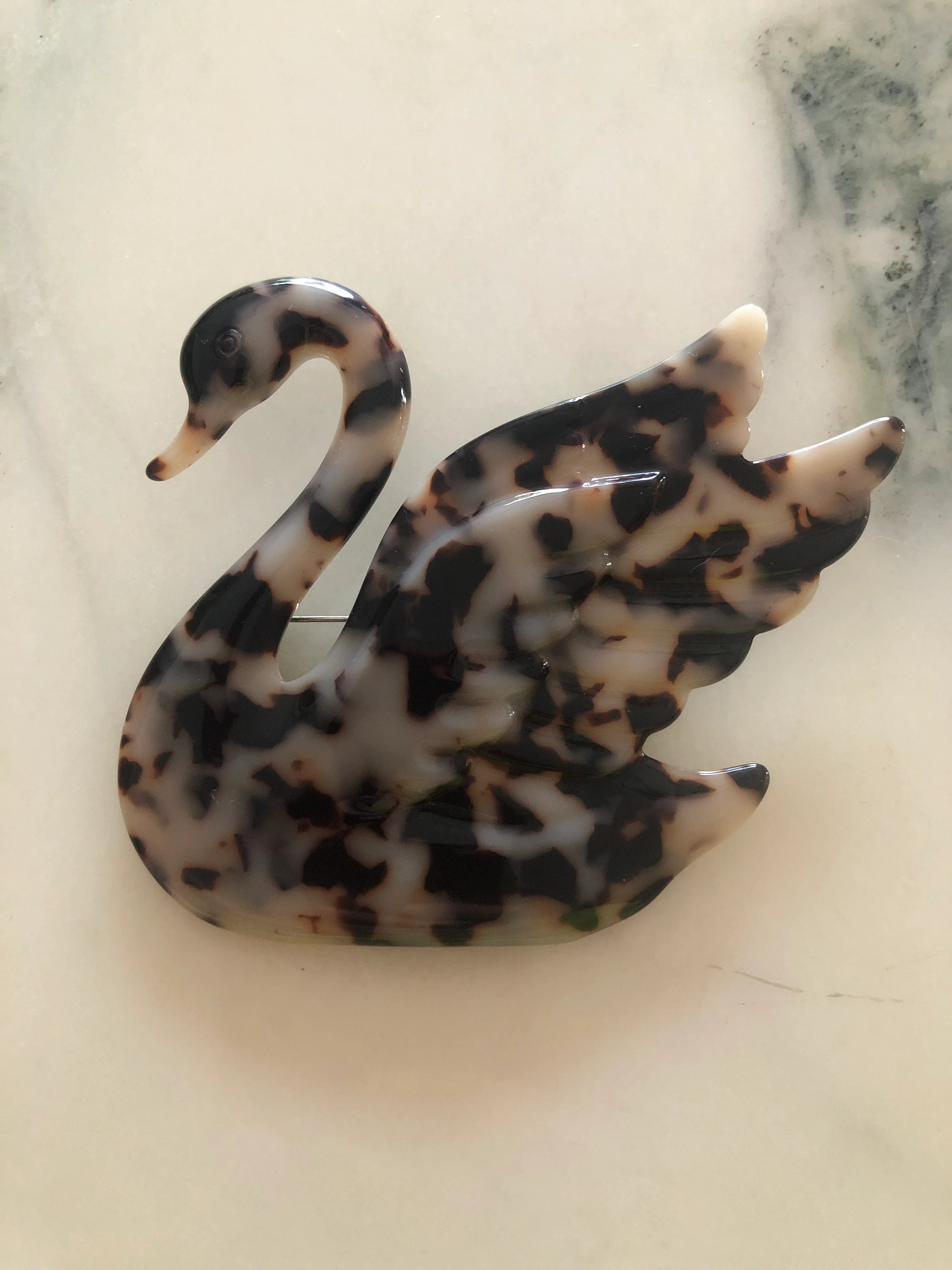 Broochella beige Animalia tortoiseshell swan shaped brooch. It is made from Premium Italian cellulose tortoiseshell acetate. It is presented on a white marble surface. 
