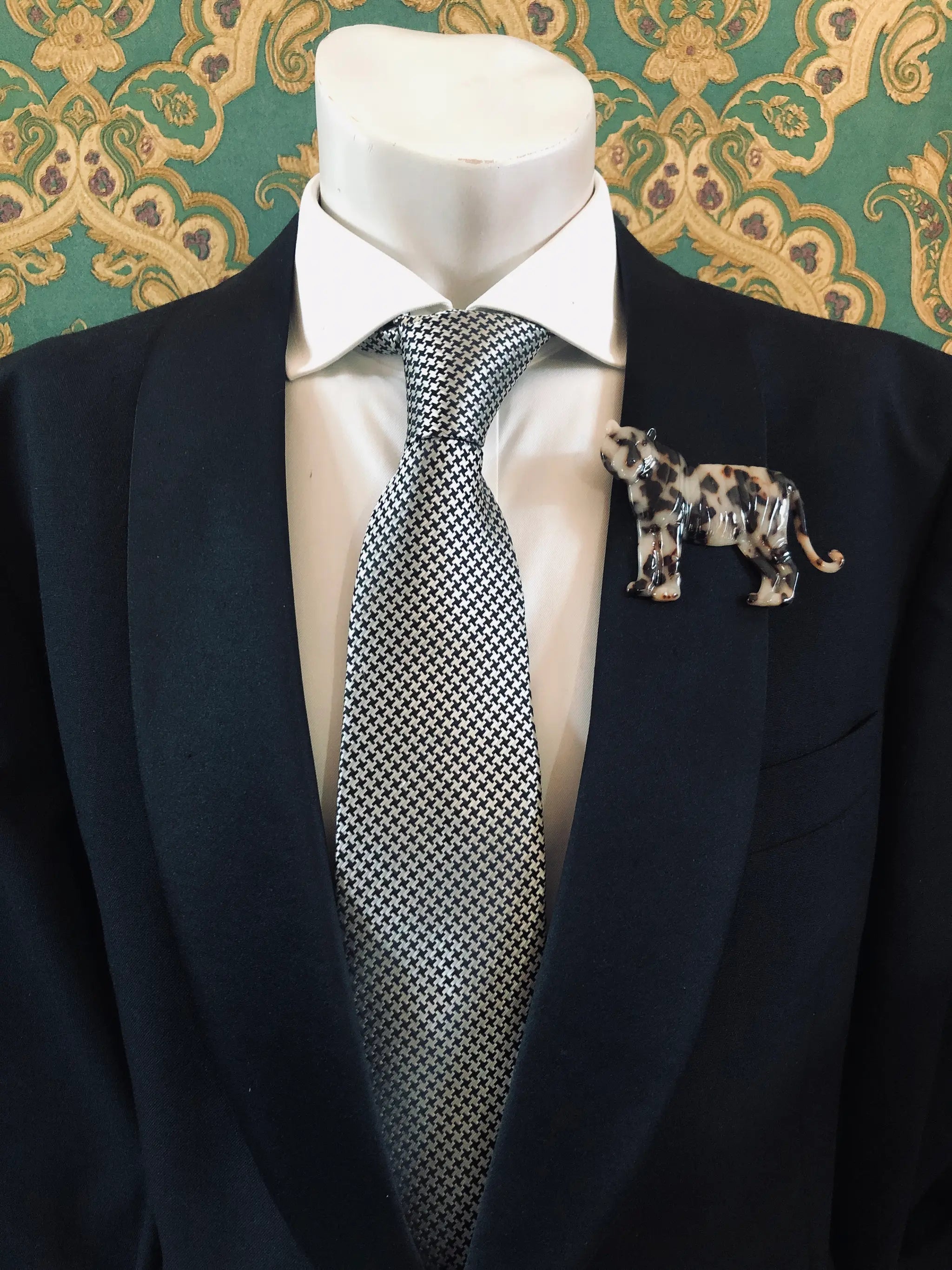 Broochella Men's beige Animalia tortoiseshell tiger shaped brooch. It is made from Premium Italian cellulose tortoiseshell acetate. It is presented on a men's mannequin that is dressed in a black suit. The background is green and gold damask wallpaper. 