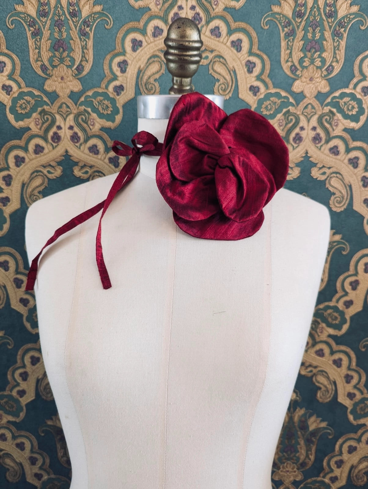 Broochella Bellucci small burgundy handmade silk flower brooch and choker  Pictured on a mannequin. The background is green and gold damask wallpaper.