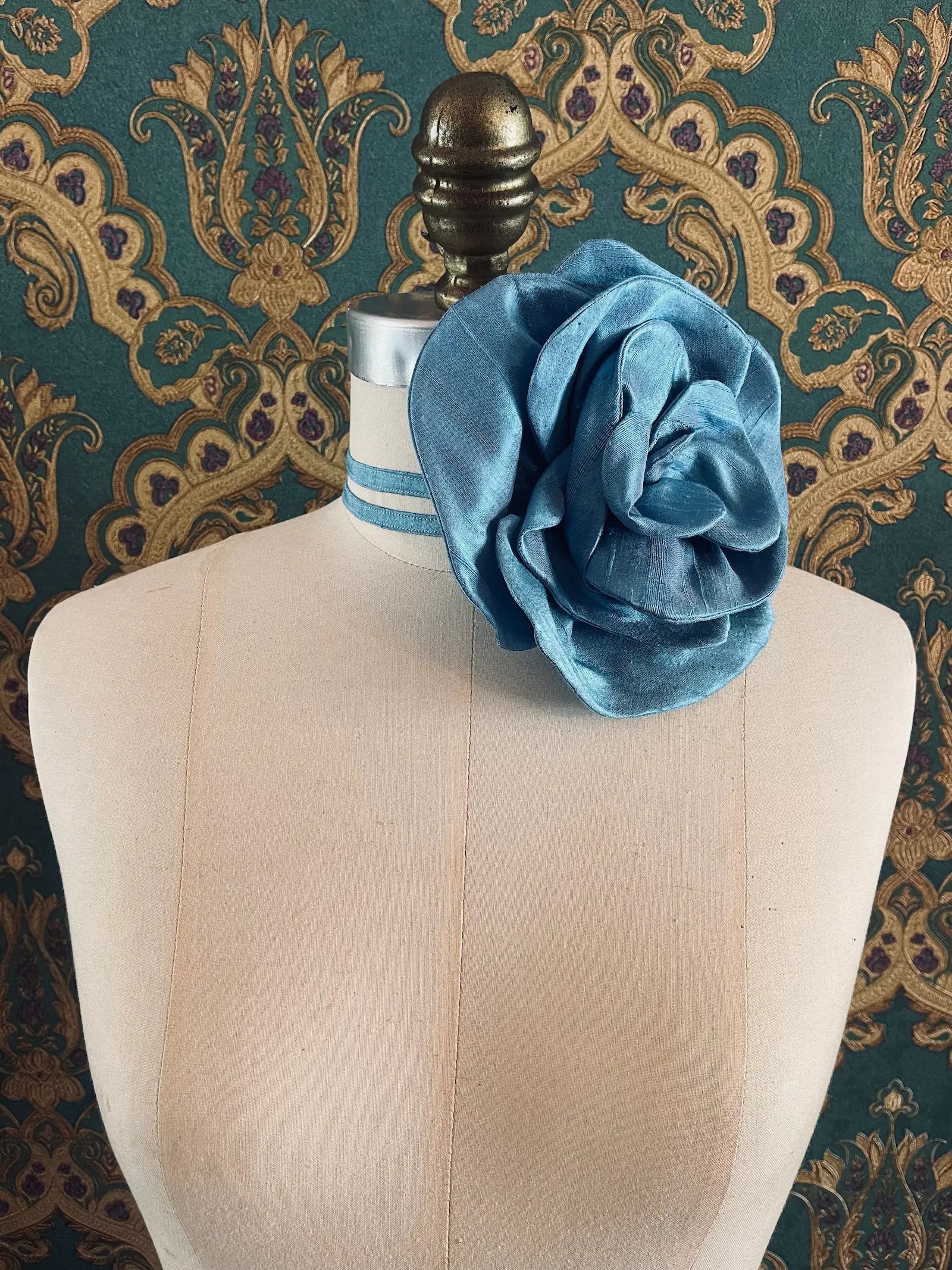 Broochella Bellucci large blue handmade silk flower brooch and choker  Pictured on a mannequin. The background is green and gold damask wallpaper.