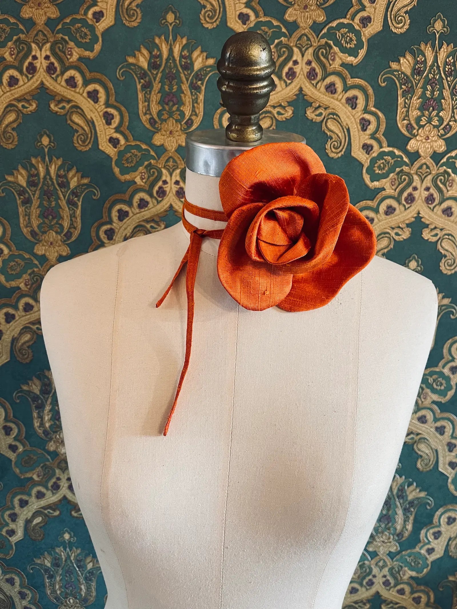Broochella Bellucci small orange handmade silk flower brooch and choker  Pictured on a mannequin. The background is green and gold damask wallpaper.