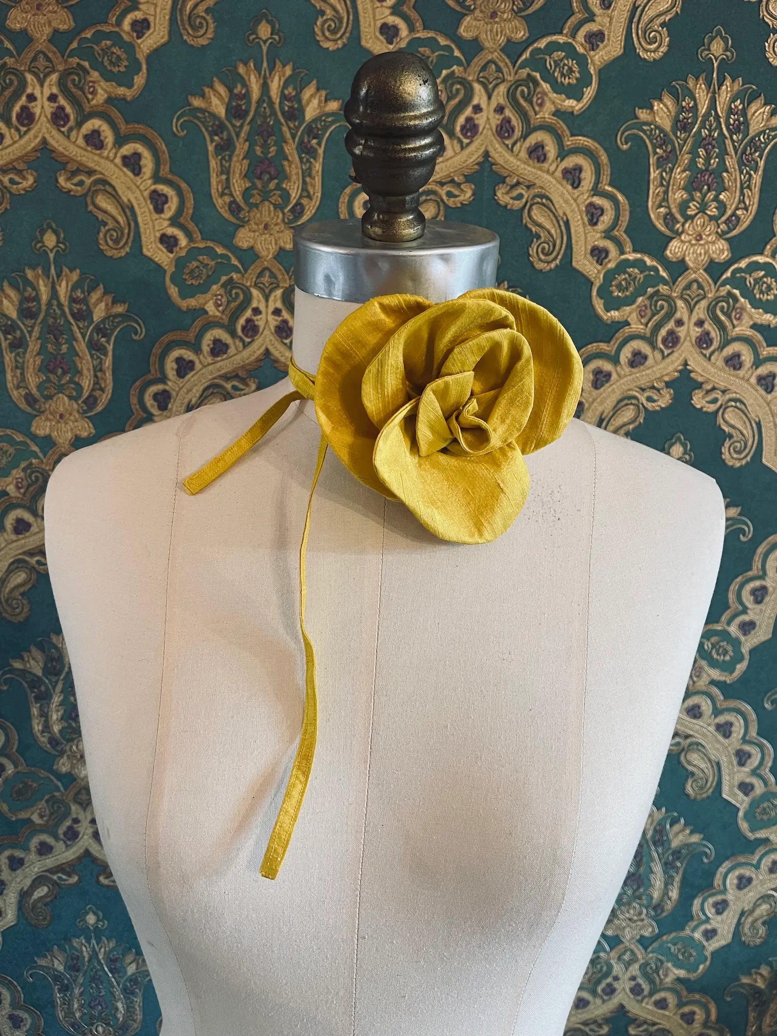 Broochella Bellucci small yellow handmade silk flower and choker  Pictured on a mannequin. The background is green and gold damask wallpaper.