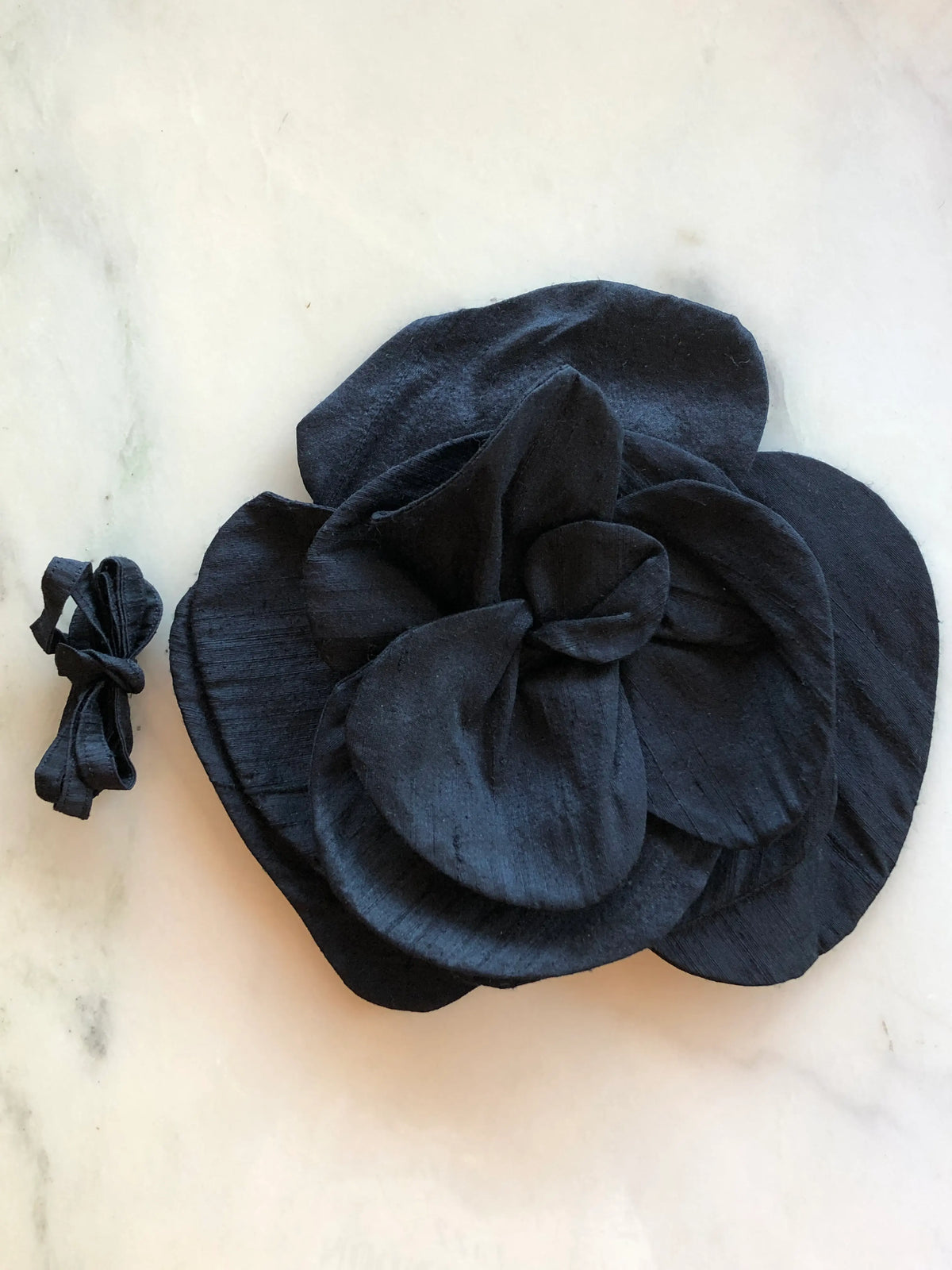 Broochella Bellucci Large Silk Flower Brooch & Choker in black, with dramatic sculptural silk petals and matching ribbon, photographed on a white marble background with subtle grey veining.