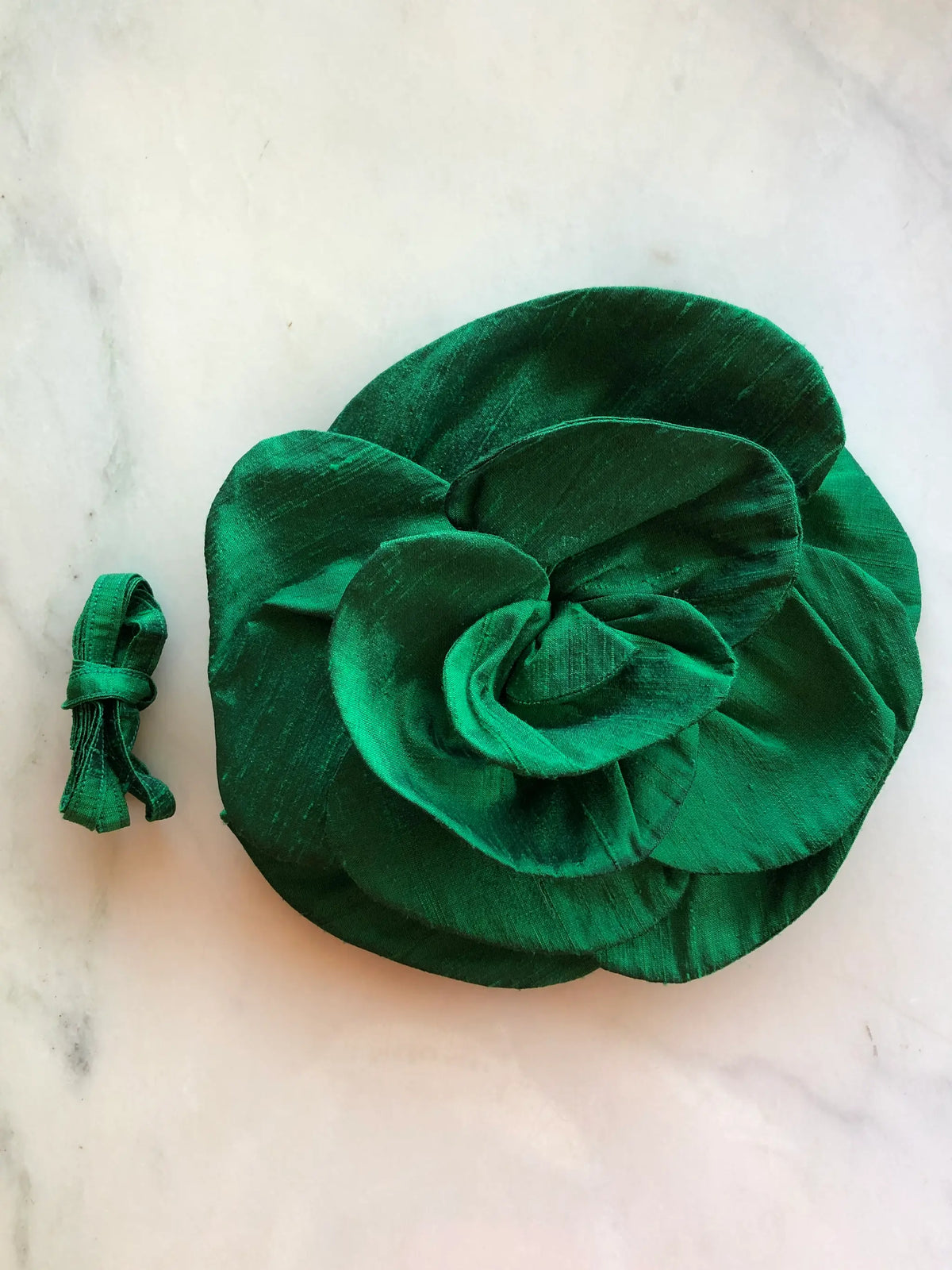 Broochella Bellucci Large Silk Flower Brooch & Choker in rich emerald green, with sculptural layered silk petals and matching ribbon, photographed on a white marble background with subtle grey veining.