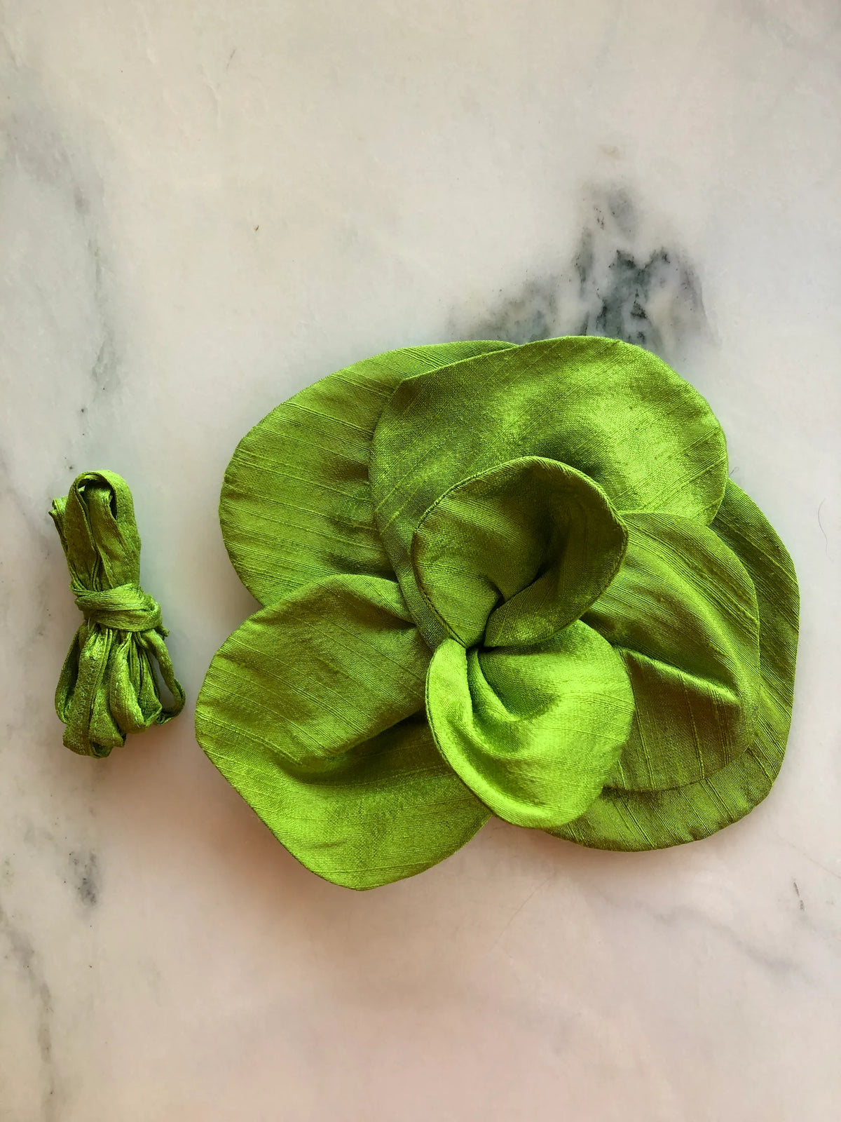Small chartreuse green Broochella Bellucci Silk-Flower Choker & Brooch with sculptural silk petals and matching silk choker ribbon, photographed on a white marble background with soft grey veining.
