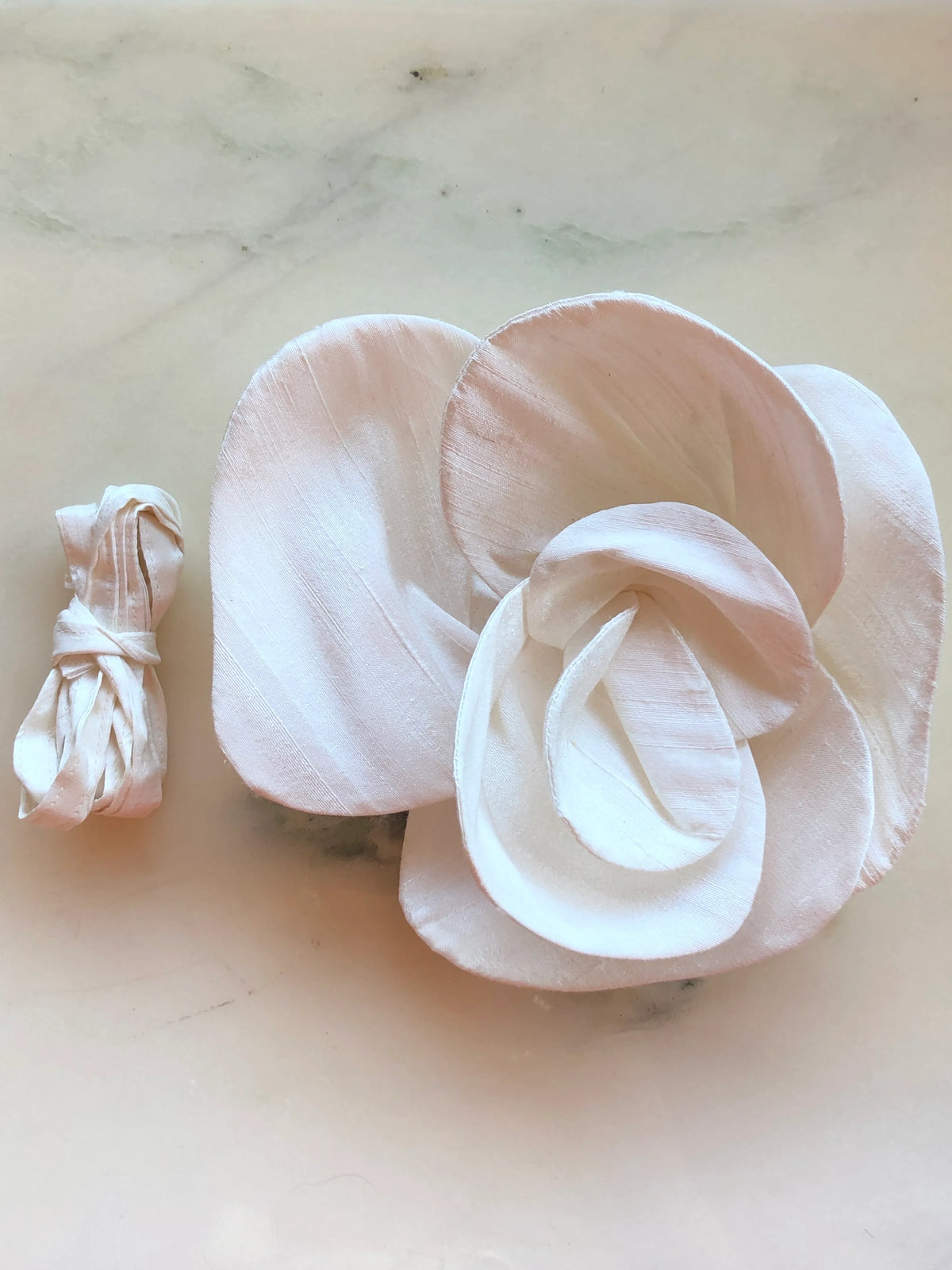 Small ivory Broochella Bellucci Silk-Flower Choker & Brooch with sculptural silk petals and matching silk choker ribbon, photographed on a white marble background with soft grey veining.
