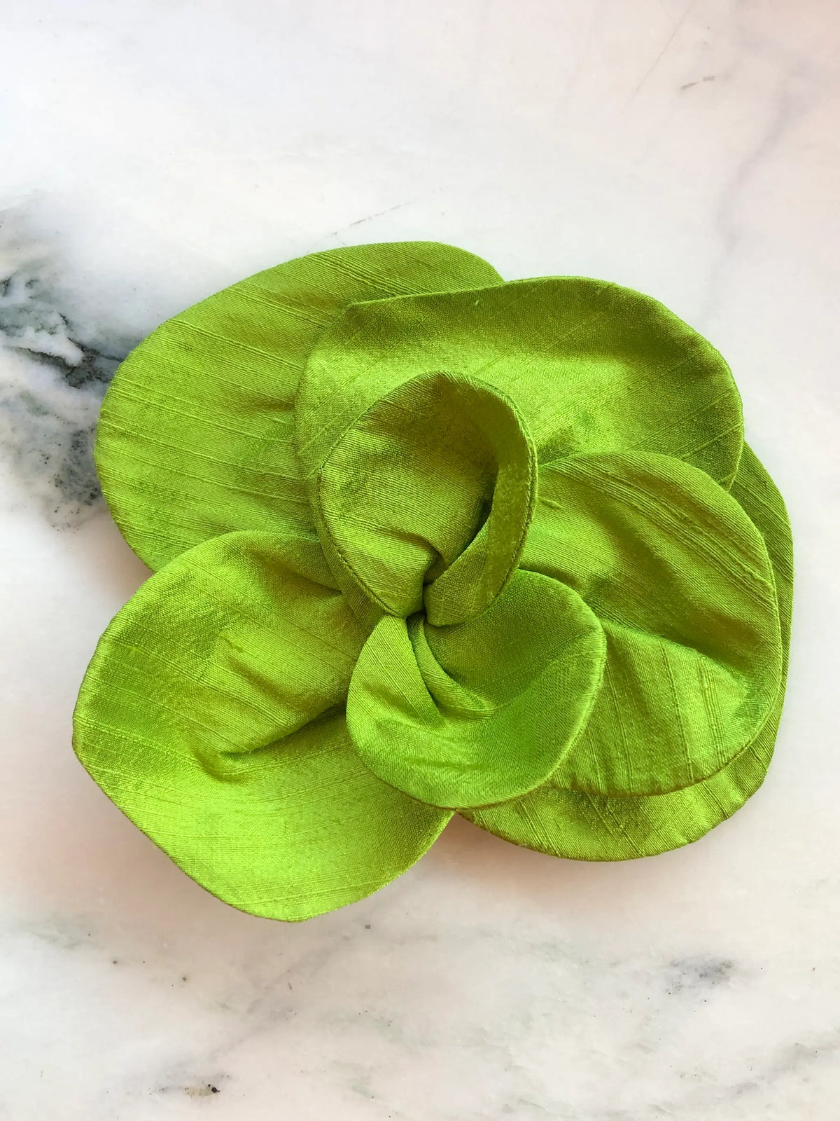 Broochella Bellucci small chartreuse silk flower brooch with sculptural layered petals and lustrous finish, photographed on a white marble background with grey veining.