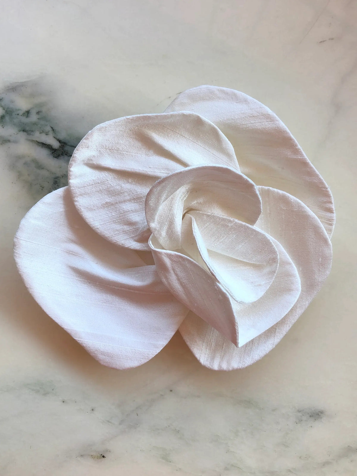 Broochella Bellucci small yellow silk flower brooch with bold layered petals and lustrous texture, photographed on a white marble background with grey veining.