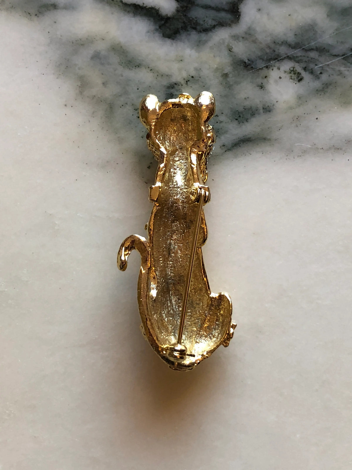Broochella Bianca Vintage Gold Cat Brooch featuring an elongated gold-tone cat with emerald-green eyes, clear crystal detailing and floral accents on a cream and grey marble background.