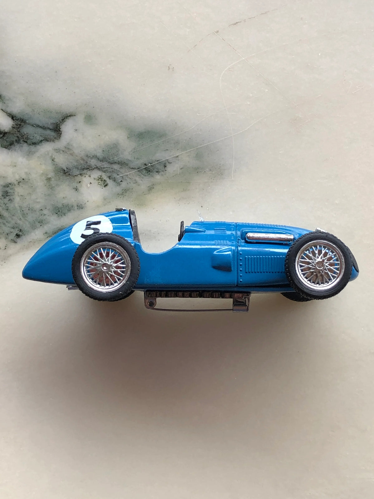 Broochella Blu Veloce No.5 Vintage Grand Prix Racing Car Brooch in side profile, featuring a bright blue vintage racing car with silver wire-spoke wheels, black tyres, open cockpit, chrome exhaust detailing and a white number 5 racing decal.