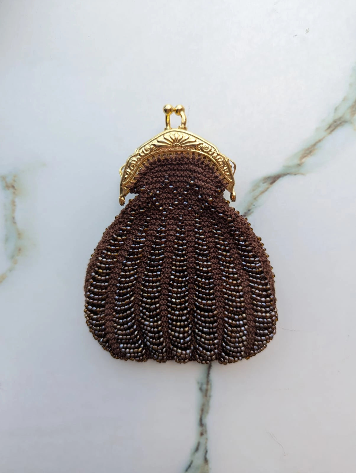 Broochella Borsellino vintage brown beaded purse brooch with gold clasp. It is pinned to a vintage mannequin. The background is a white marble.