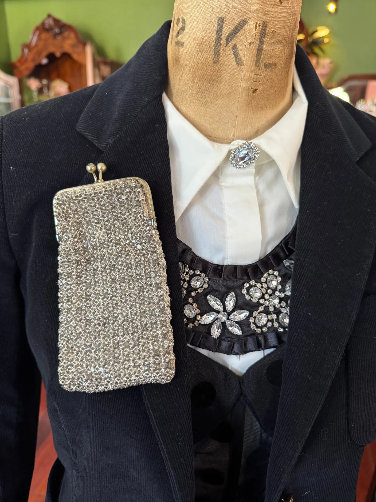Mannequin wearing a black coat with a sparkling handbag and white shirt with decorative collar. It is wearing the Broochella Borsellino vintage crystal purse brooch. 
