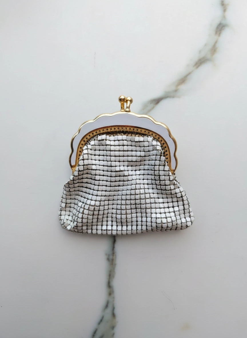 Broochella Borsellino vintage, white, glomesh purse brooch. It has a gold and white metal frame and clasp. The background is white marble. 
