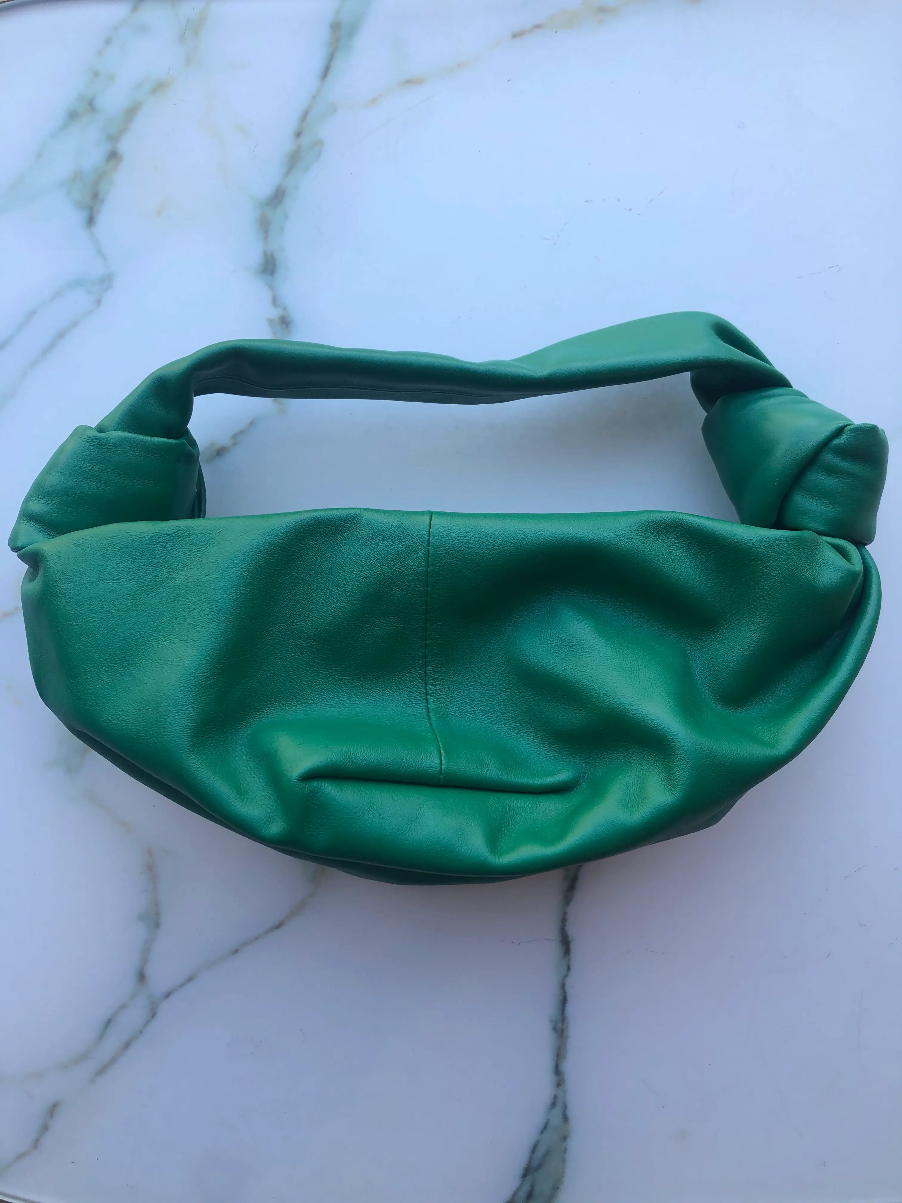 Broochella Bottega veneta mini double knot bag in green leather. It is presented on a white marble background.