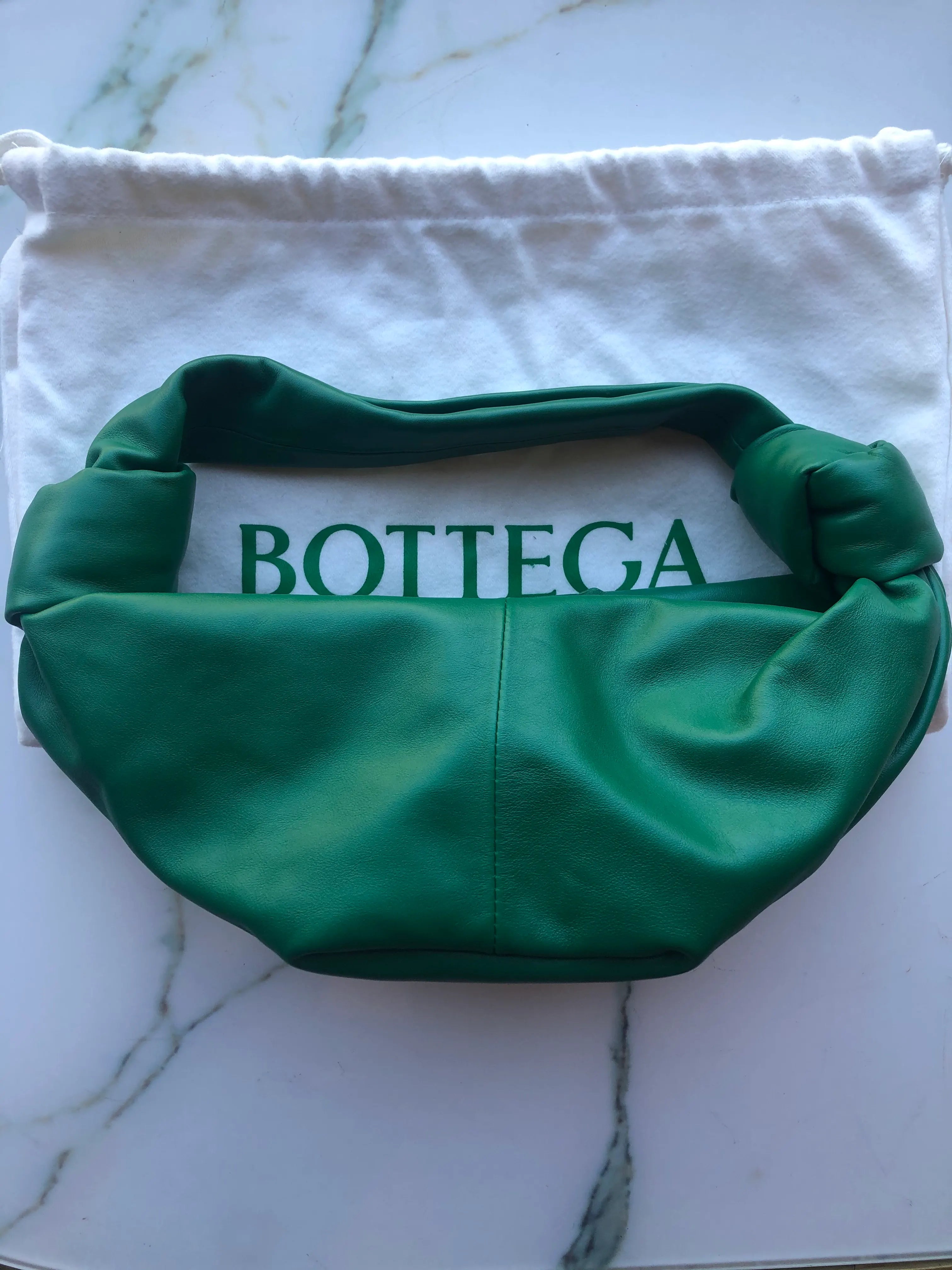 Broochella Bottega veneta mini double knot bag in green leather. It is presented on a white marble background.