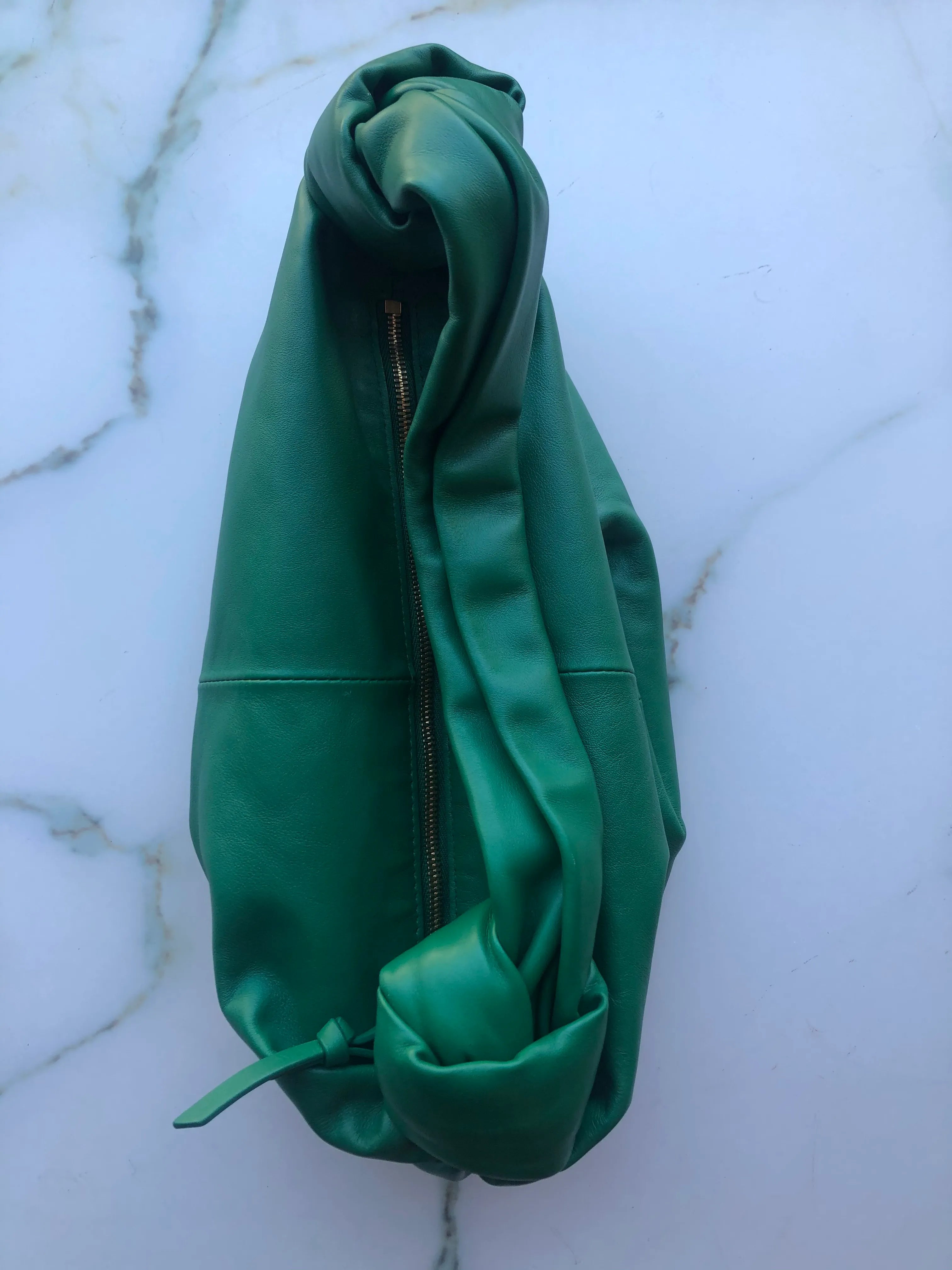 Broochella Bottega veneta mini double knot bag in green leather. It is presented on a white marble background.
