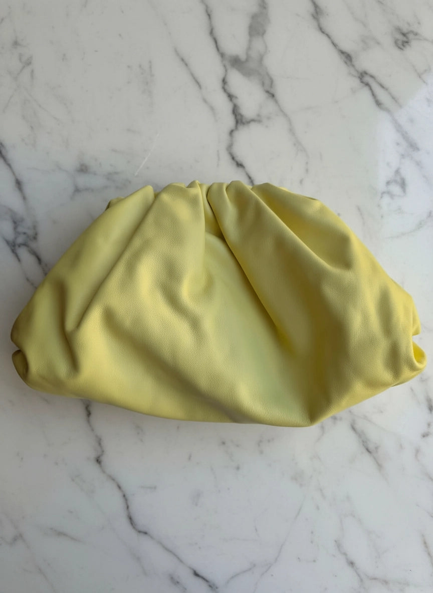 A Broochella Bottega Veneta The Pouch pale yellow large leather pouch clutch bag purse  with gathered pleats, placed on a white marble surface with gray veining.