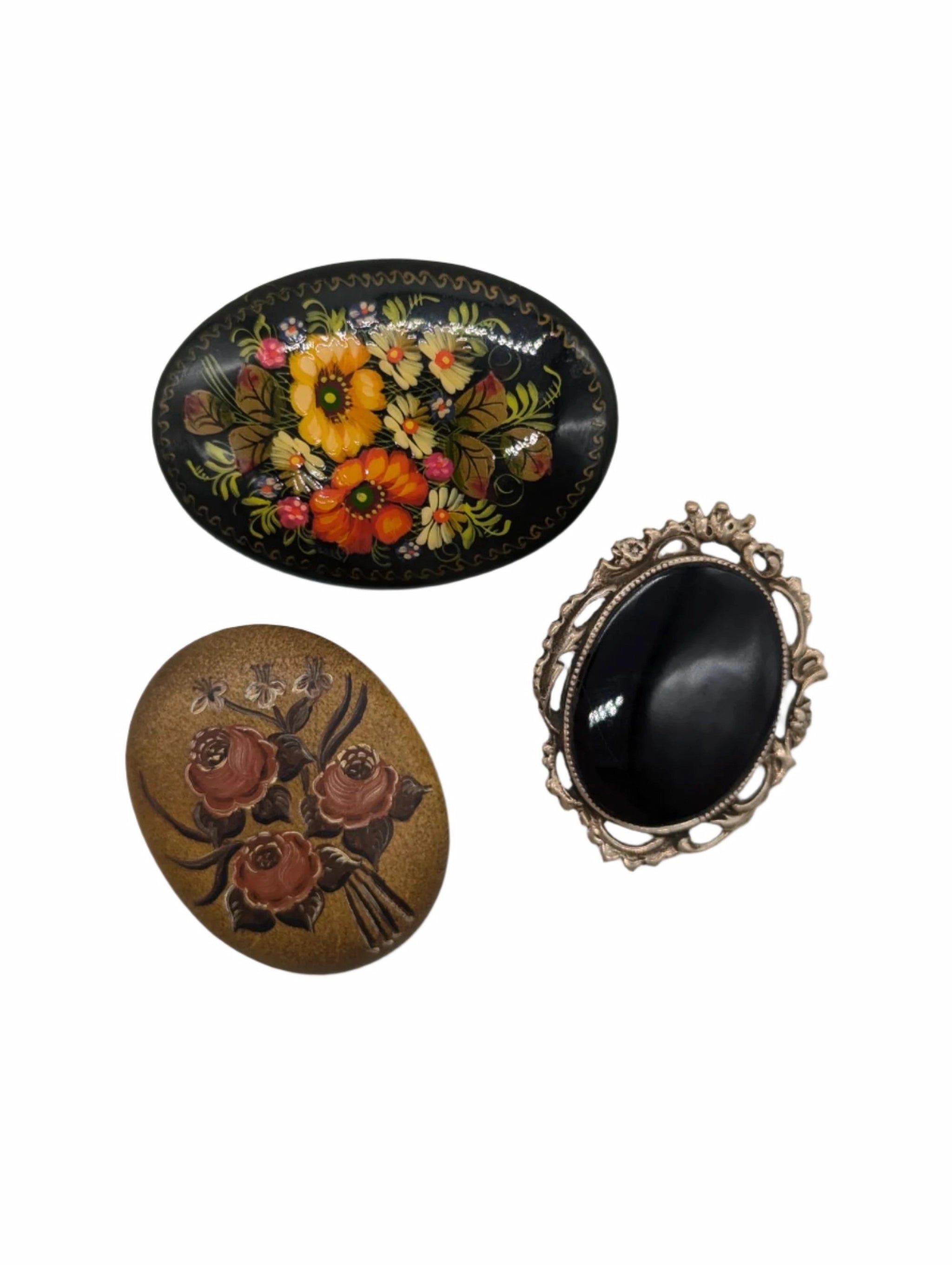 Broochella Botticini vintage brooch set. There are three oval shaped brooches.  Two have flowers painted on them. One is black, with a silver metal frame. The background is white. 