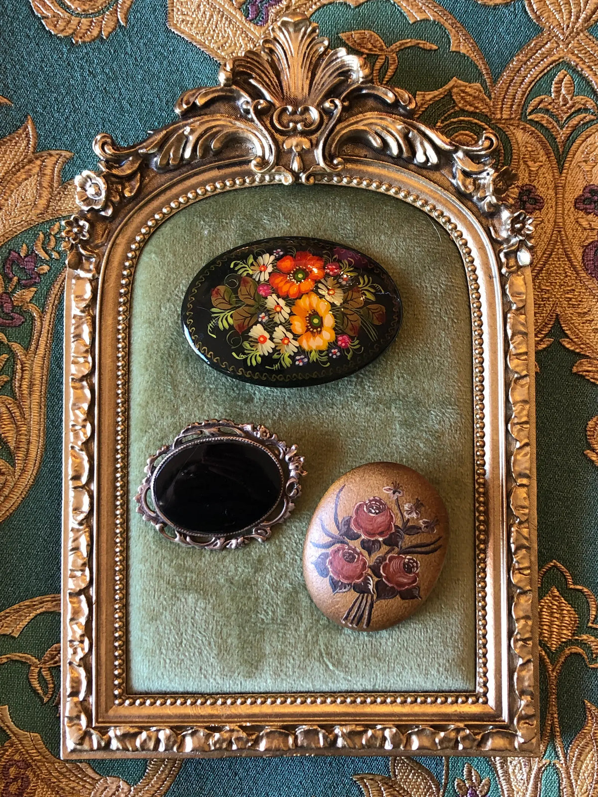 Broochella Botticini Vintage Brooch Trio featuring three oval floral and black statement brooches displayed on sage green velvet in an ornate gold frame against a teal and gold patterned background.