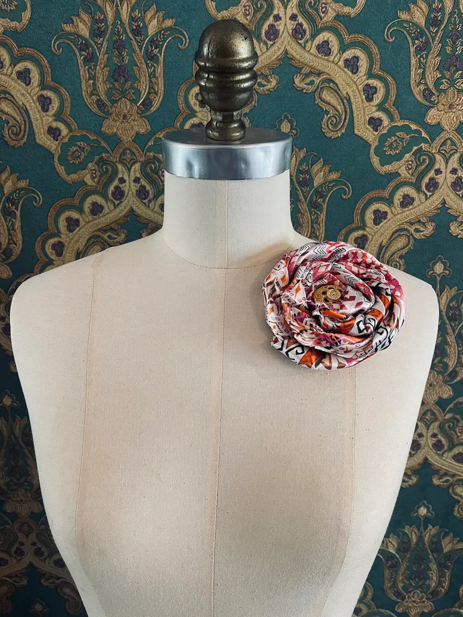 Broochella bougainville handmade pink designer satin flower brooch pictured on a mannequin the background is green and gold damask wallpaper
