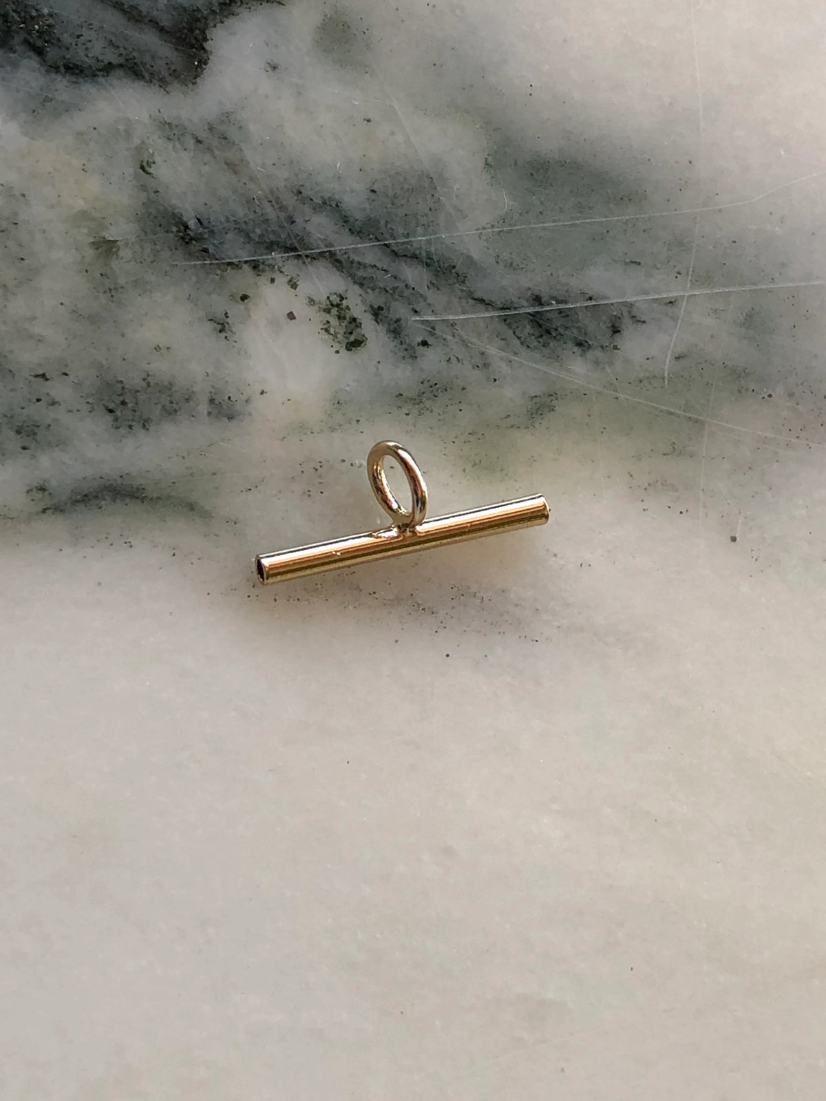 Broochella extended bar brooch to necklace converter in gold-tone metal with central oval loop, photographed on white marble with grey-green veining.