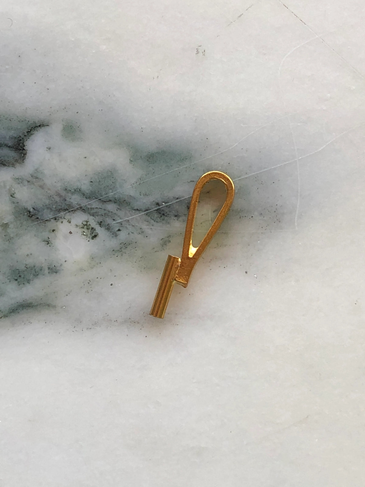 Broochella vertical brooch to necklace converter in gold-tone metal with elongated loop design, photographed on white marble with grey-green veining.