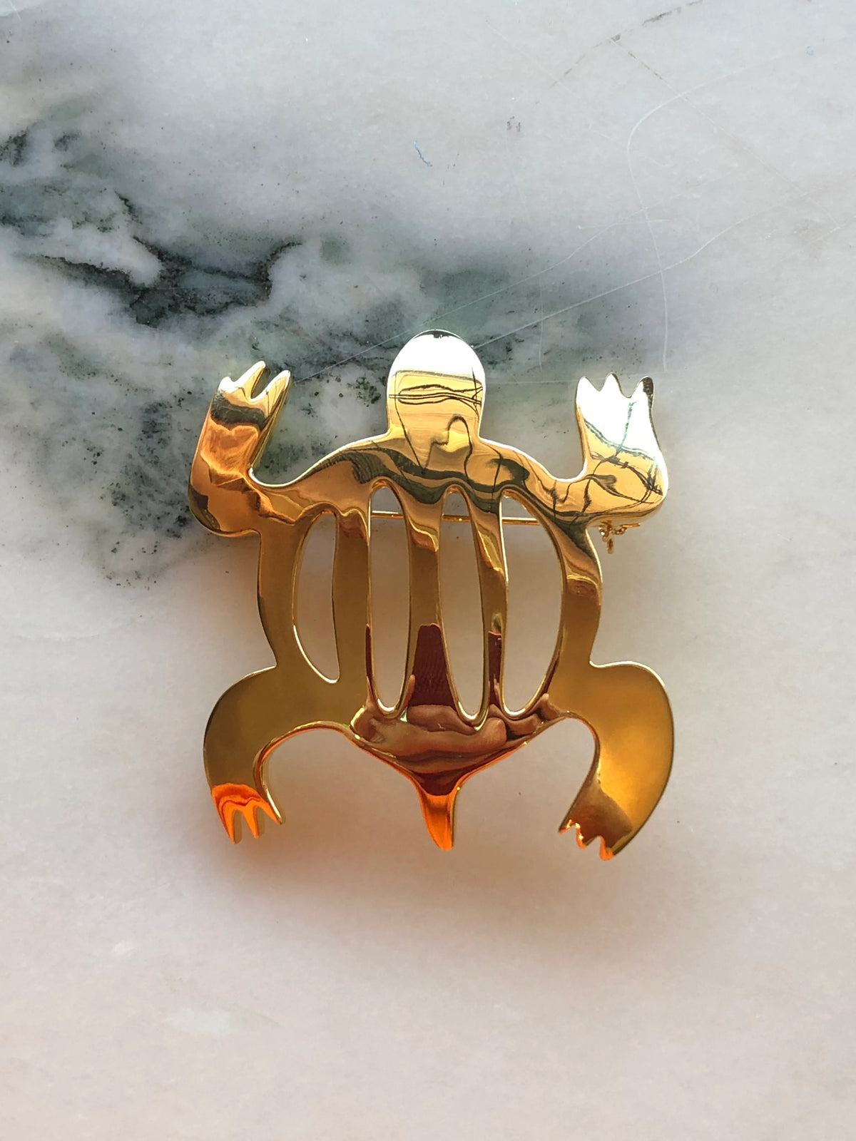 Broochella Brooches with Meaning Brooch Pin – Adaptability, featuring an abstract polished gold-tone figure with sculptural cut-out detailing on a cream marble background.