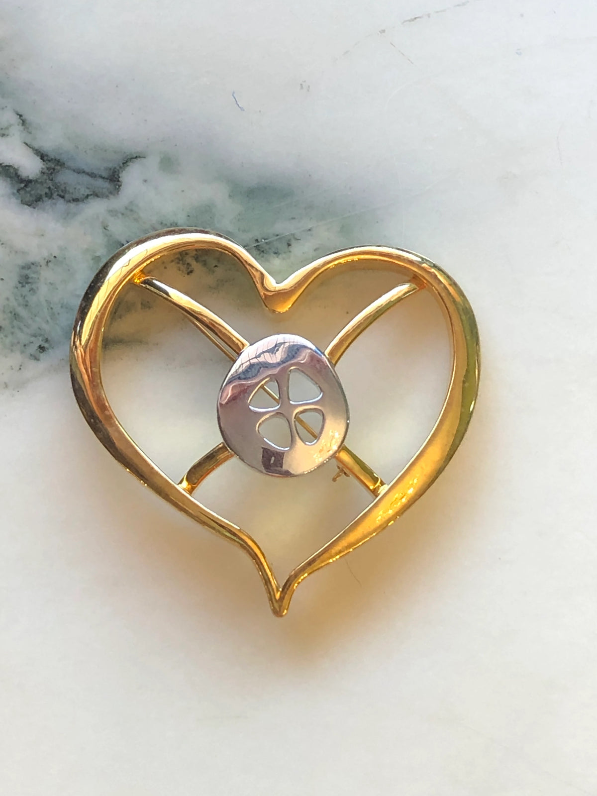 Broochella Brooches with Meaning – Hope Brooch Pin, featuring a polished gold-tone open heart design with a contrasting silver-tone centre and four-petal cut-out detail on a cream marble background.