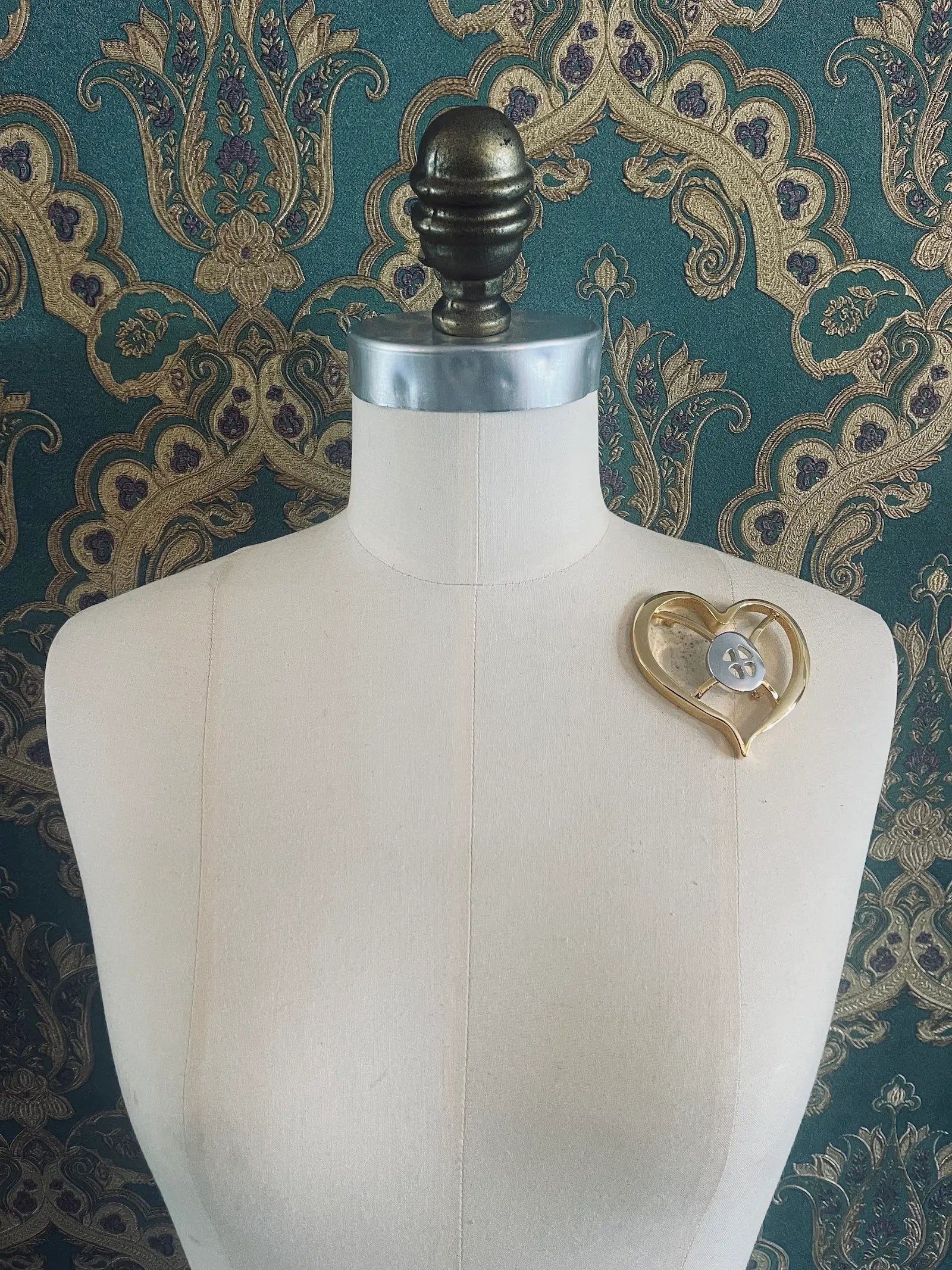 Broochella Brooches with meaning designer gold and silver metal hope brooch. Pictured on a mannequin. The background is green and gold damask wallpaper