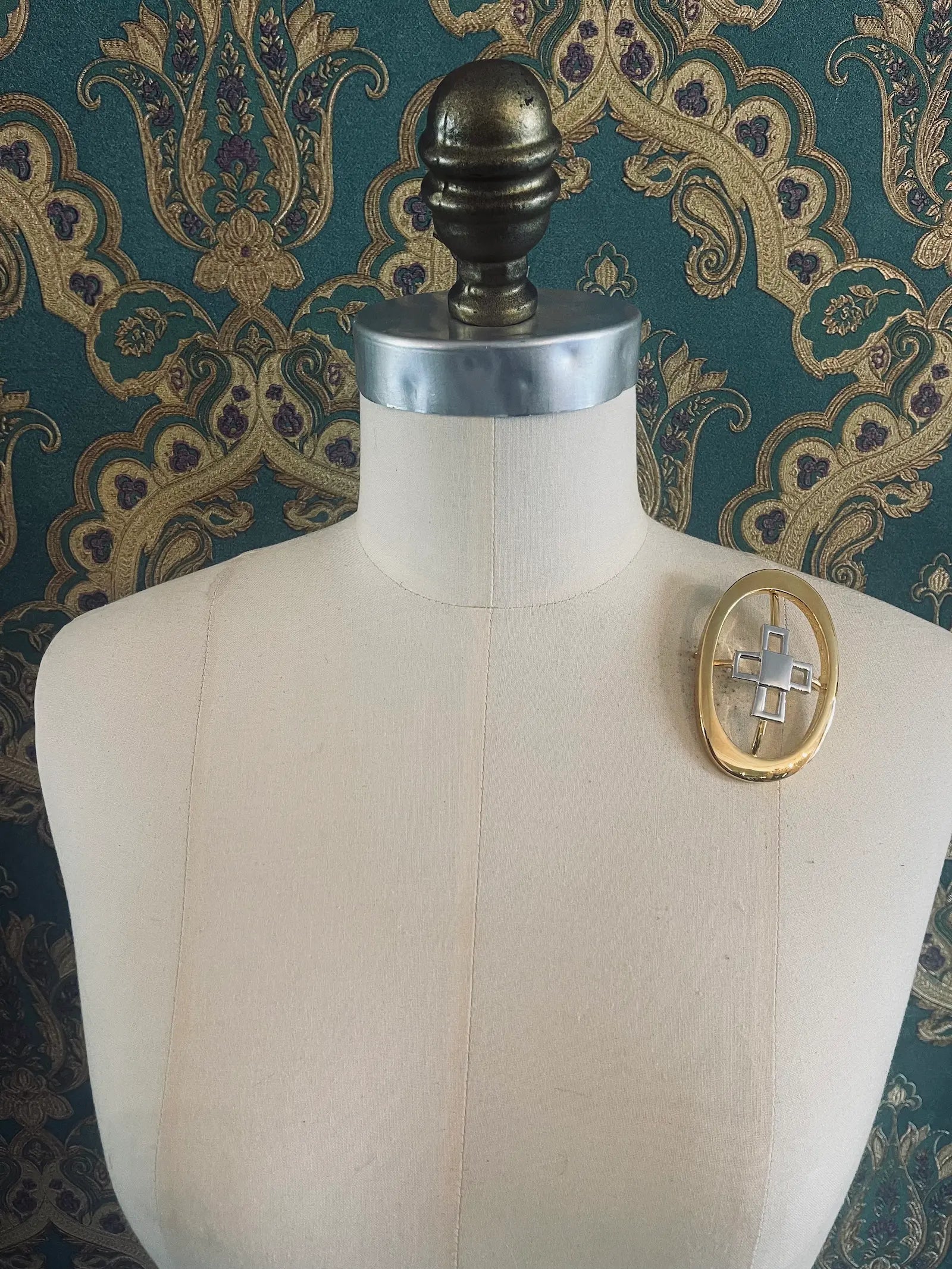 Broochella Brooches with meaning designer gold and silver metal knowledge brooch. Pictured on a mannequin. The background is green and gold damask wallpaper