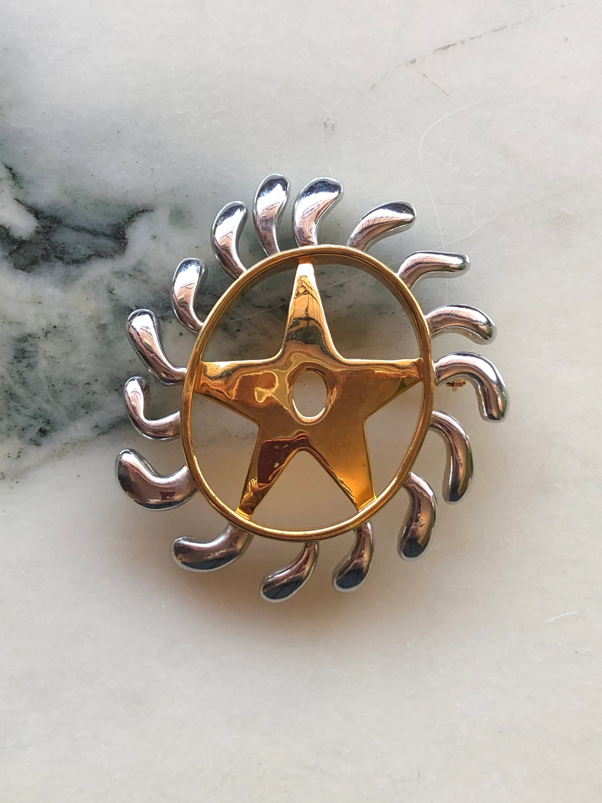 Broochella Brooches with Meaning – Welcoming Change brooch in polished gold and silver-tone metal, featuring a symbolic figure surrounded by radiating curved forms.