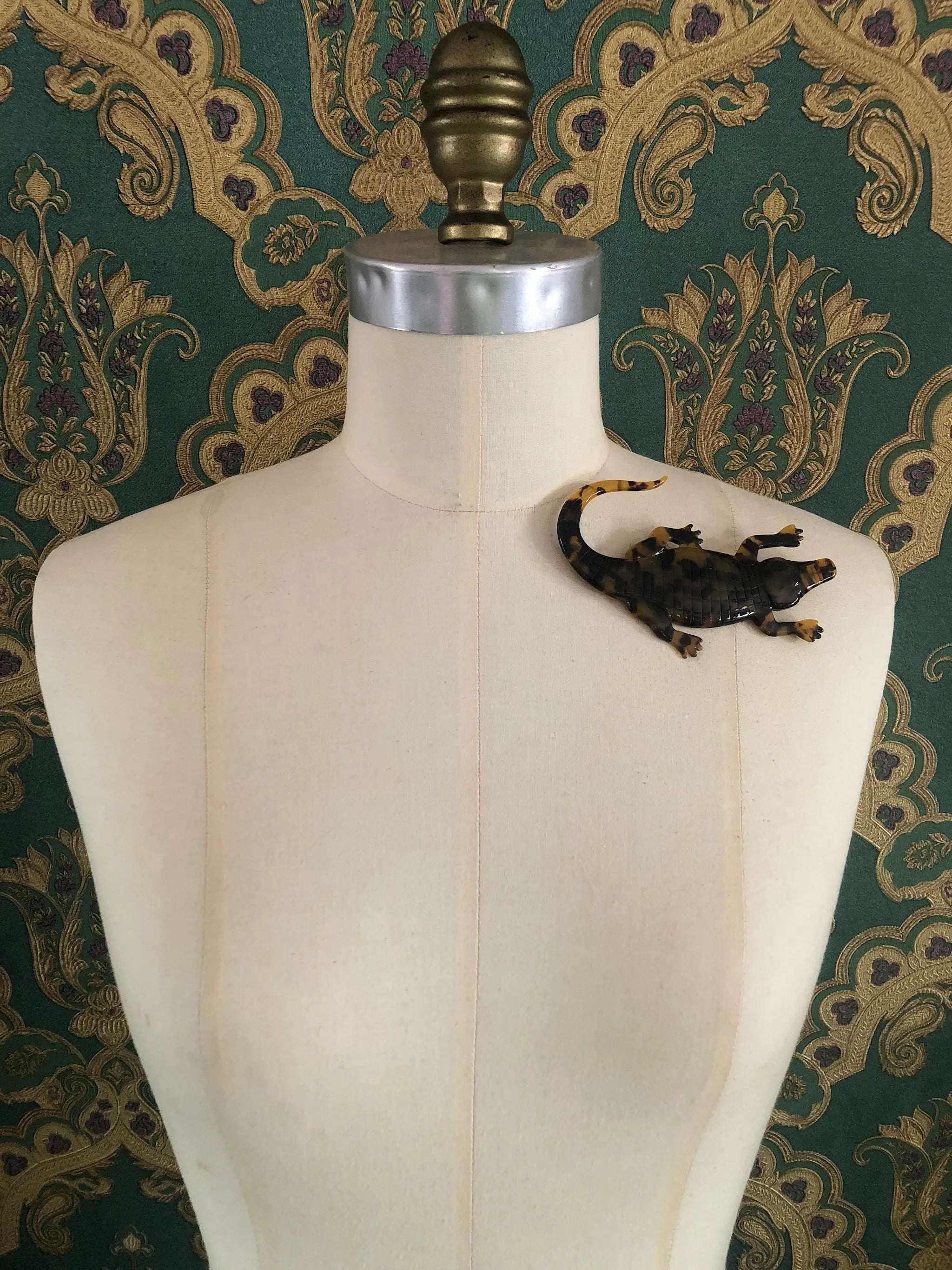 Broochella animalia collection brown and black tortoiseshell crocodile handmade designer cellulose acetate brooch.  Pictured on a mannequin.  The background is green and gold damask wallpaper