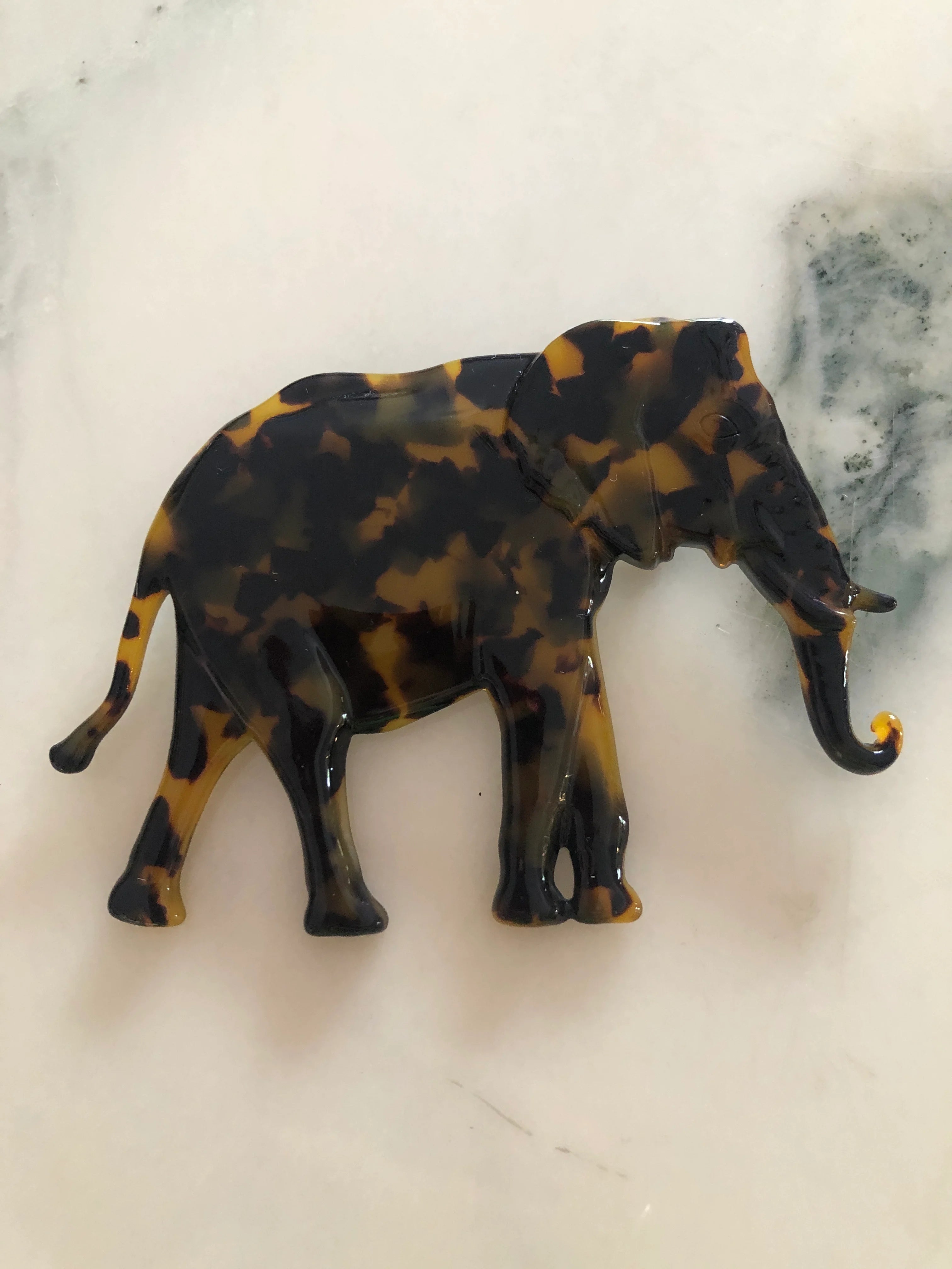Broochella Men's beige Animalia tortoiseshell giraffe shaped brooch. It is made from Premium Italian cellulose tortoiseshell acetate. It is presented on a white marble table.