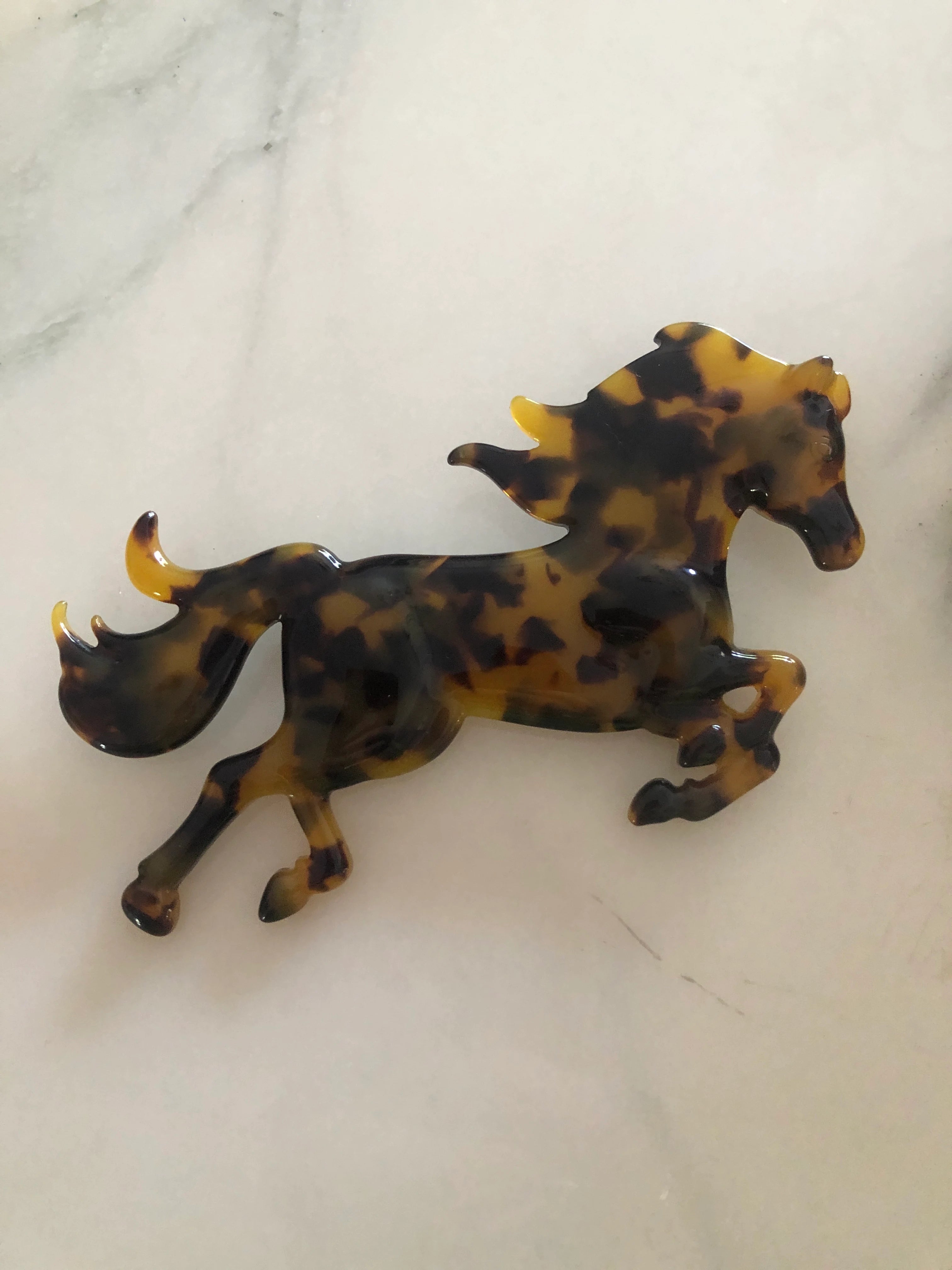 Broochella Animalia Collection black and brown tortoiseshell horse brooch. It is made from premium, Italian cellulose acetate. The background is white marble. 