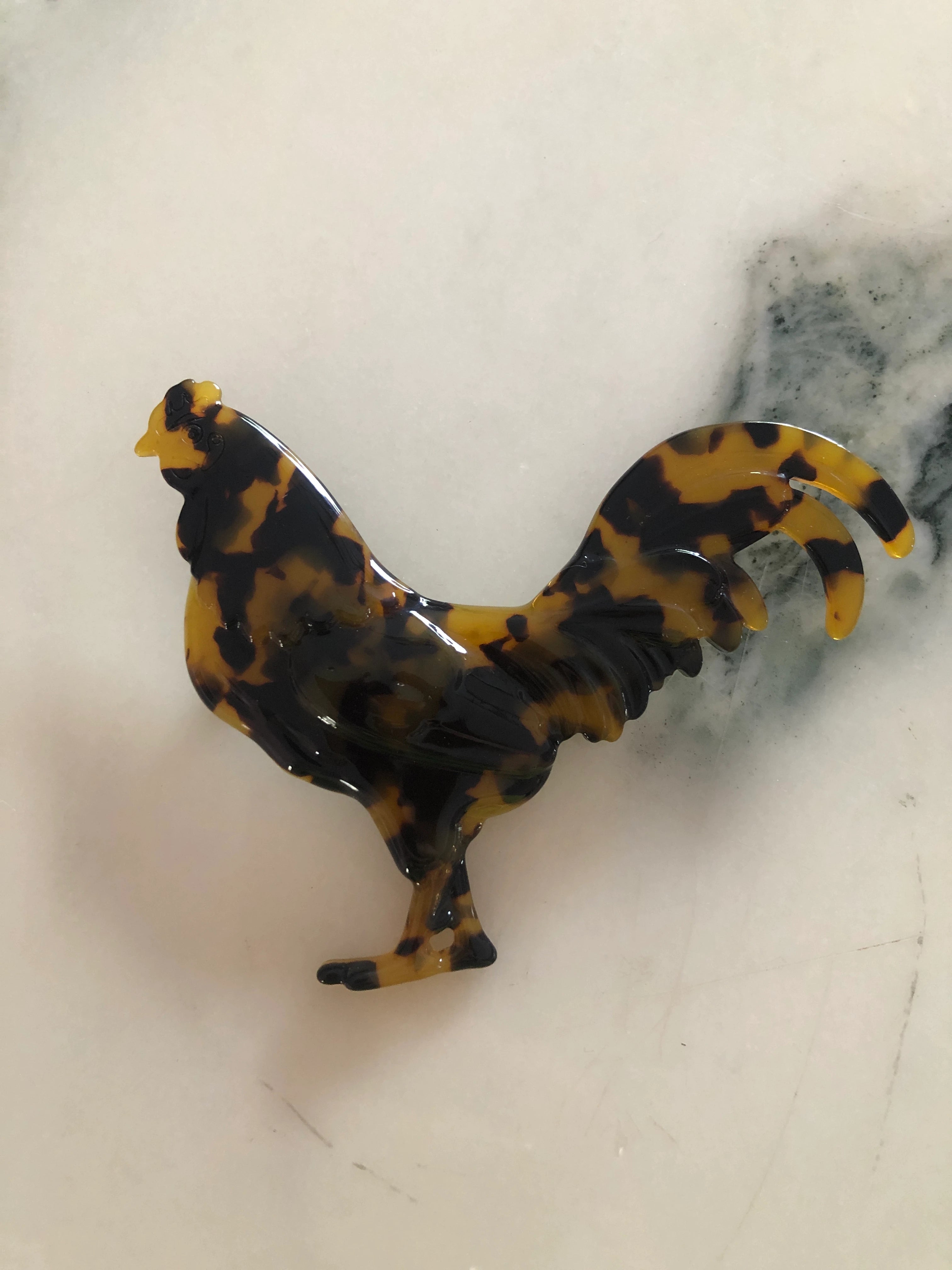 Broochella Animalia handmade, tortoiseshell, Italian cellulose acetate rooster brooch in beige. The background is white marble.