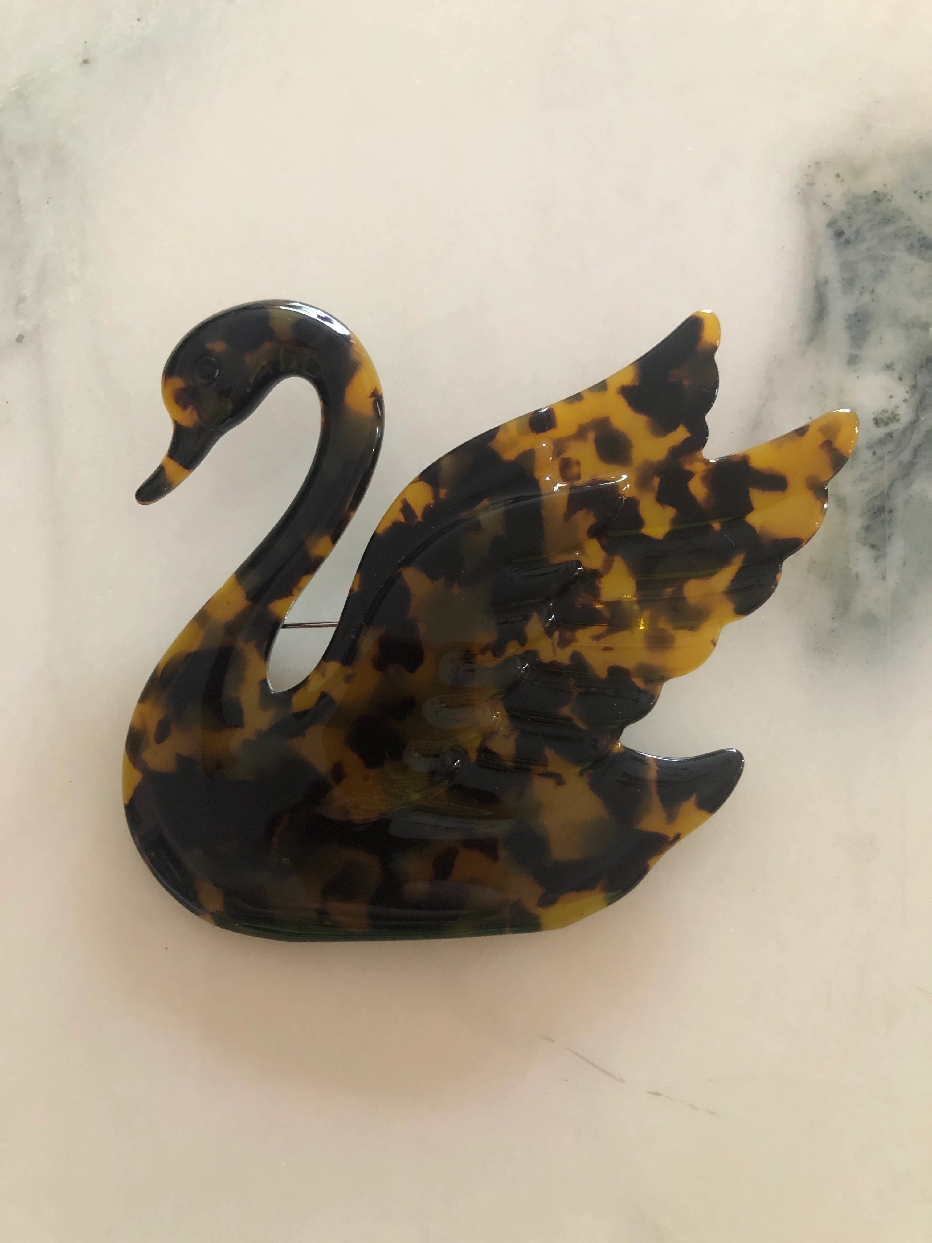 Broochella beige Animalia tortoiseshell swan shaped brooch. It is made from Premium Italian cellulose tortoiseshell acetate. It is presented on a white marble surface. 