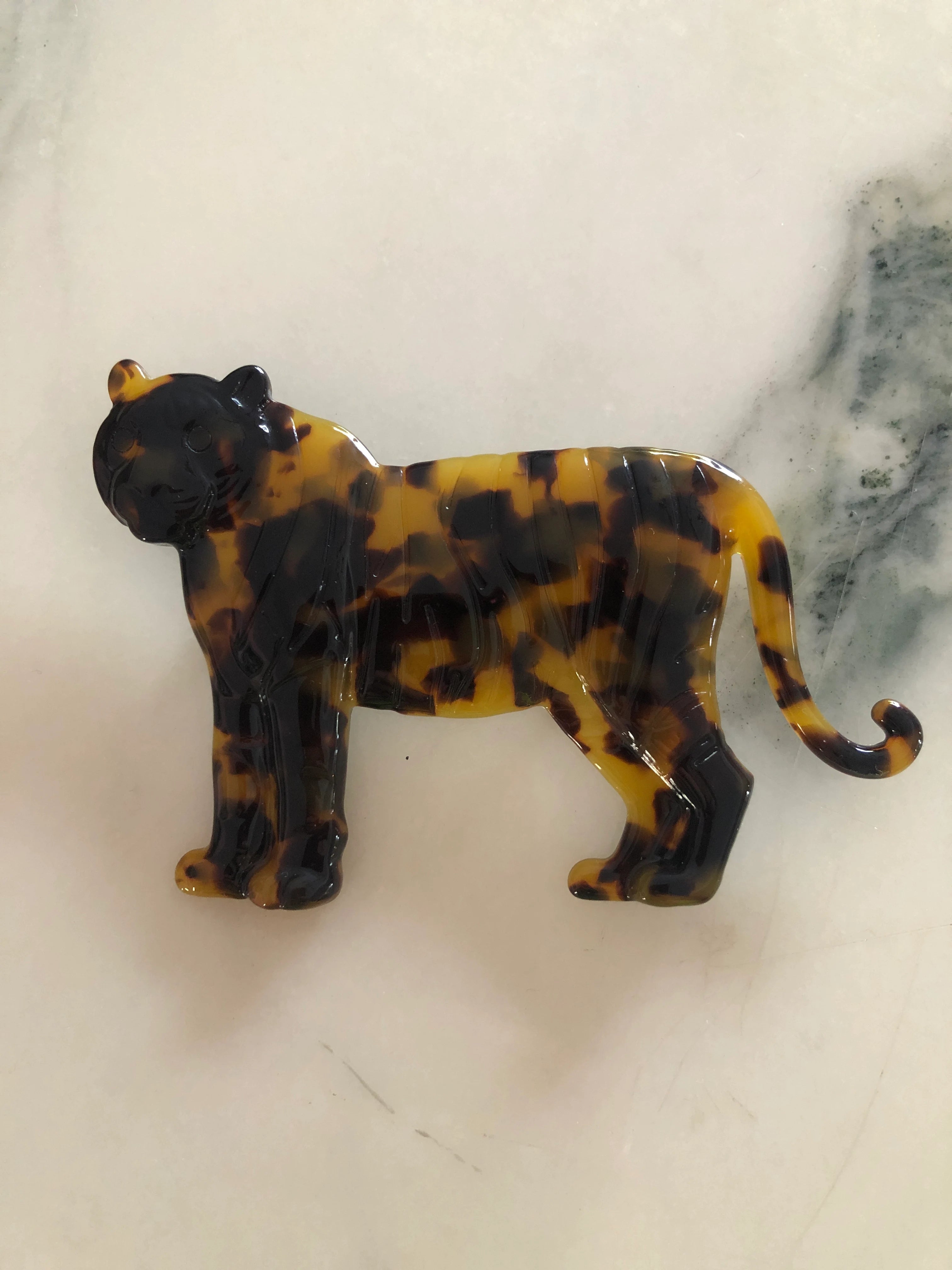 Broochella Men's brown Animalia tortoiseshell tiger shaped brooch. It is made from Premium Italian cellulose tortoiseshell acetate. It is presented on a white marble surface.