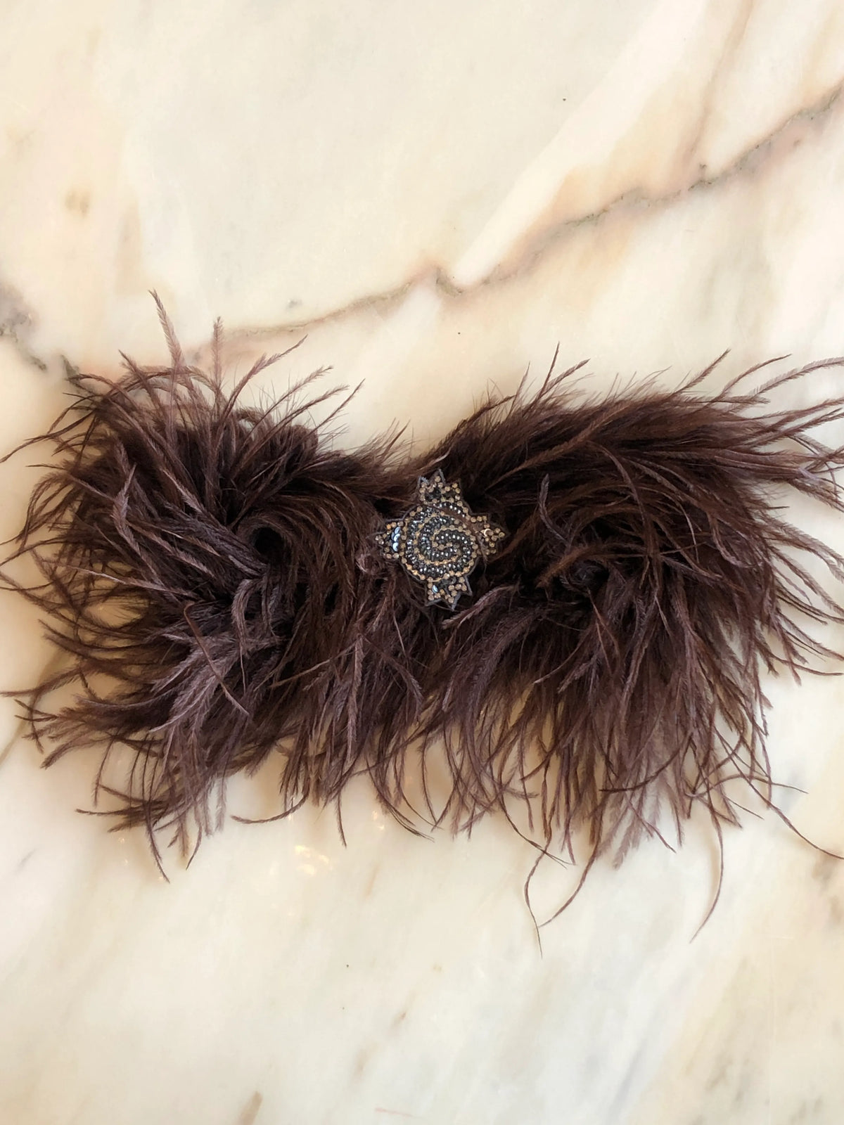 Broochella handmade Brown Feather Bow Brooch featuring dramatic ostrich feathers and an ornate jewelled centre, an oversized designer statement fashion accessory photographed on a white marble background.