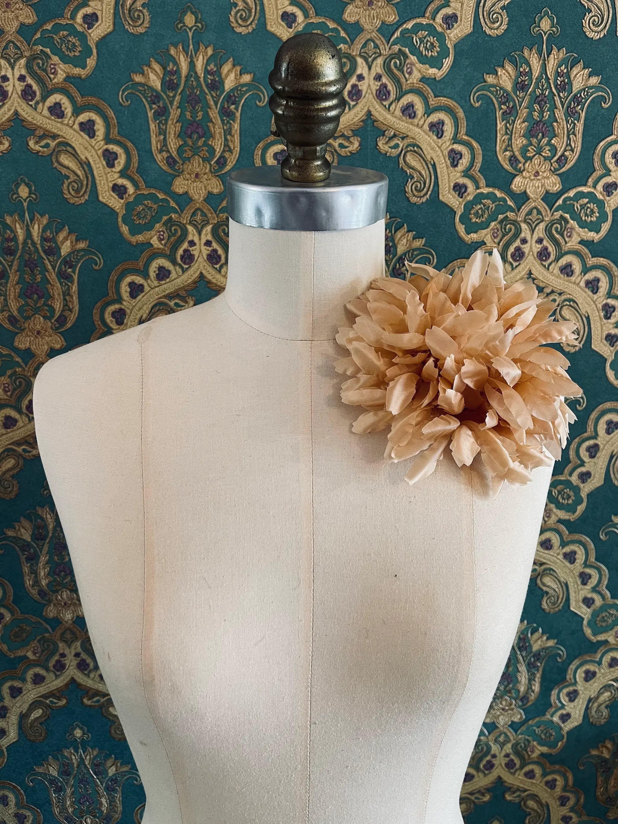 Broochella Calendula handmade fabric flower brooch. Styled on a mannequin. The background is green and gold damask wallpaper