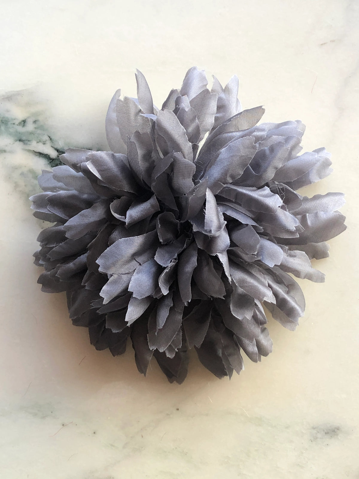Broochella Men's Calendula Handmade Flower Brooch featuring layered grey fabric petals in a full sculptural floral design, photographed on a cream marble background.