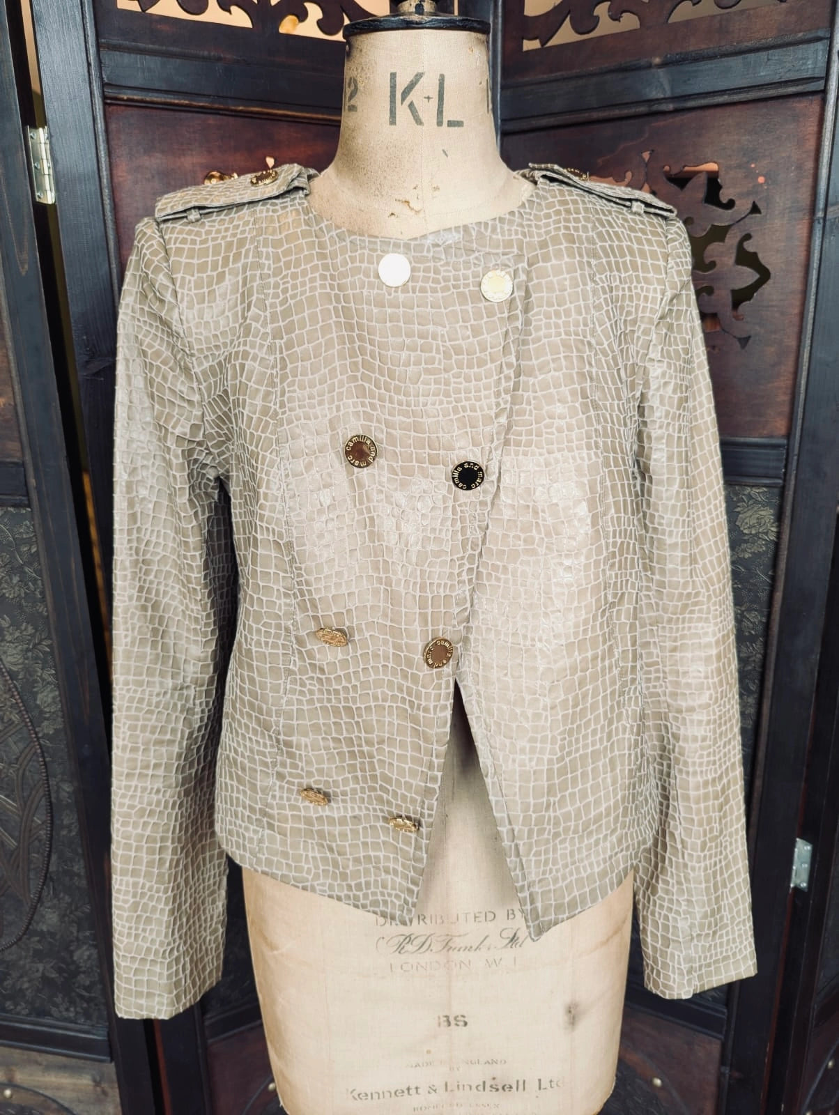 A Broochella Camilla & Marc cropped, double-breasted jacket with a textured, crocodile-embossed pattern in beige and brown, displayed on a vintage cream-coloured mannequin dress form against a dark wooden background.