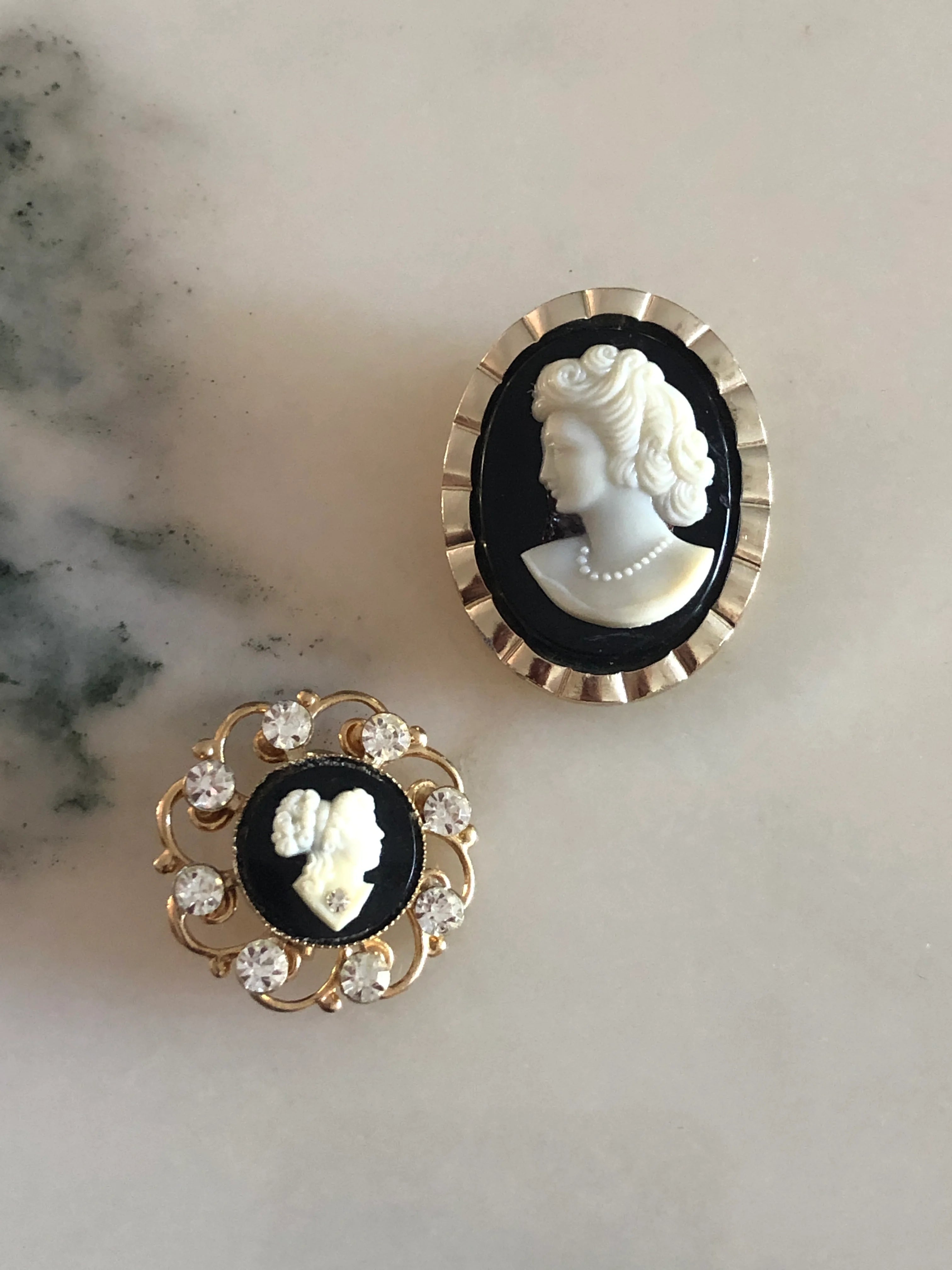 Broochella Cavaliere vintage cameo tie clip and brooch set. They are black and white with decorative metal frames. They are displayed on a white marble table