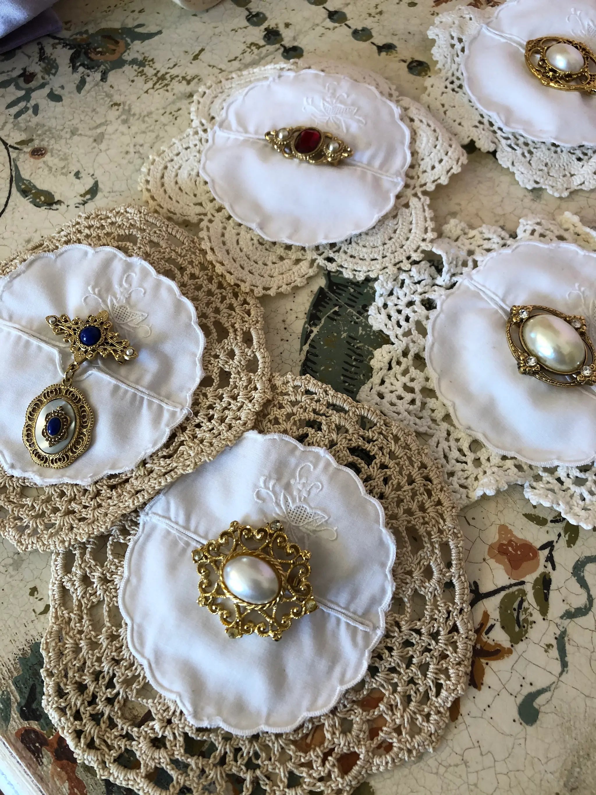 Broochella Correedi white fabric brooches  with pearl-like centers and ornate gold-tone brooch settings, arranged over a floral surface.