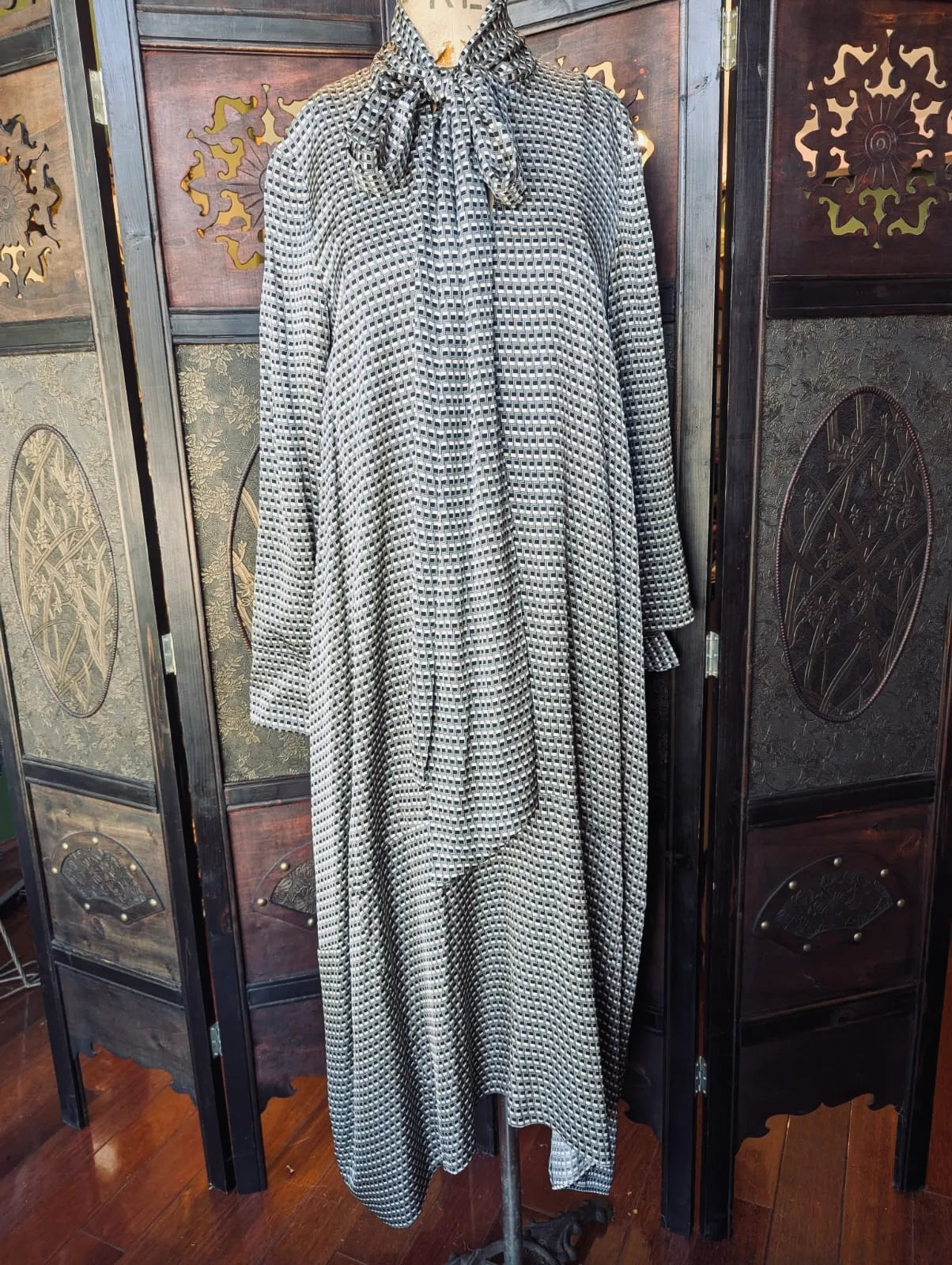 COS Black & Cream Patterned Dress – Size 34. Black and white print, long sleeve dress, with long sleeves and an neck tie. It is pictured on a mannequin. The background is an ornate, dark wood screen. 