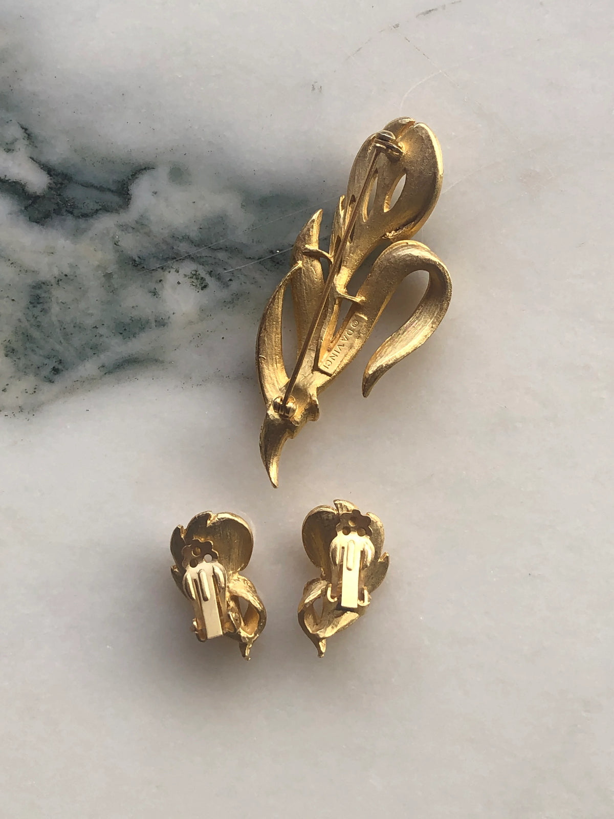 Broochella Da Vinci Vintage Brooch and Clip-on Earring Set back view showing the brooch pin and clip-on earring fastenings, photographed on a white marble background with soft grey-green veining.