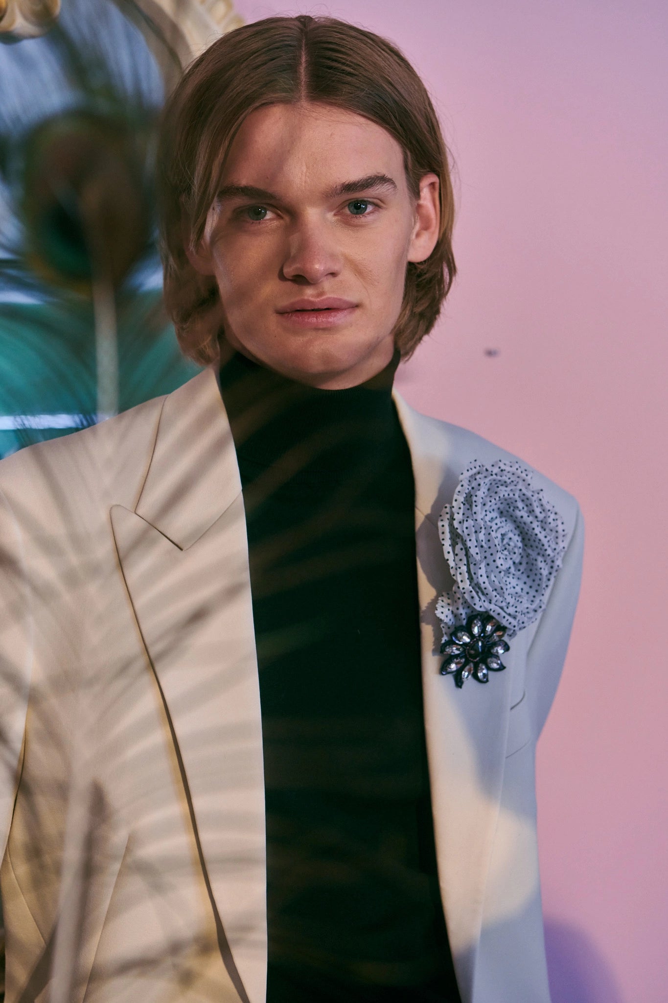 Broochella dalmata flower brooch on a male model. He is wearing a white dinner jacket and is standing in front of a pink wall.