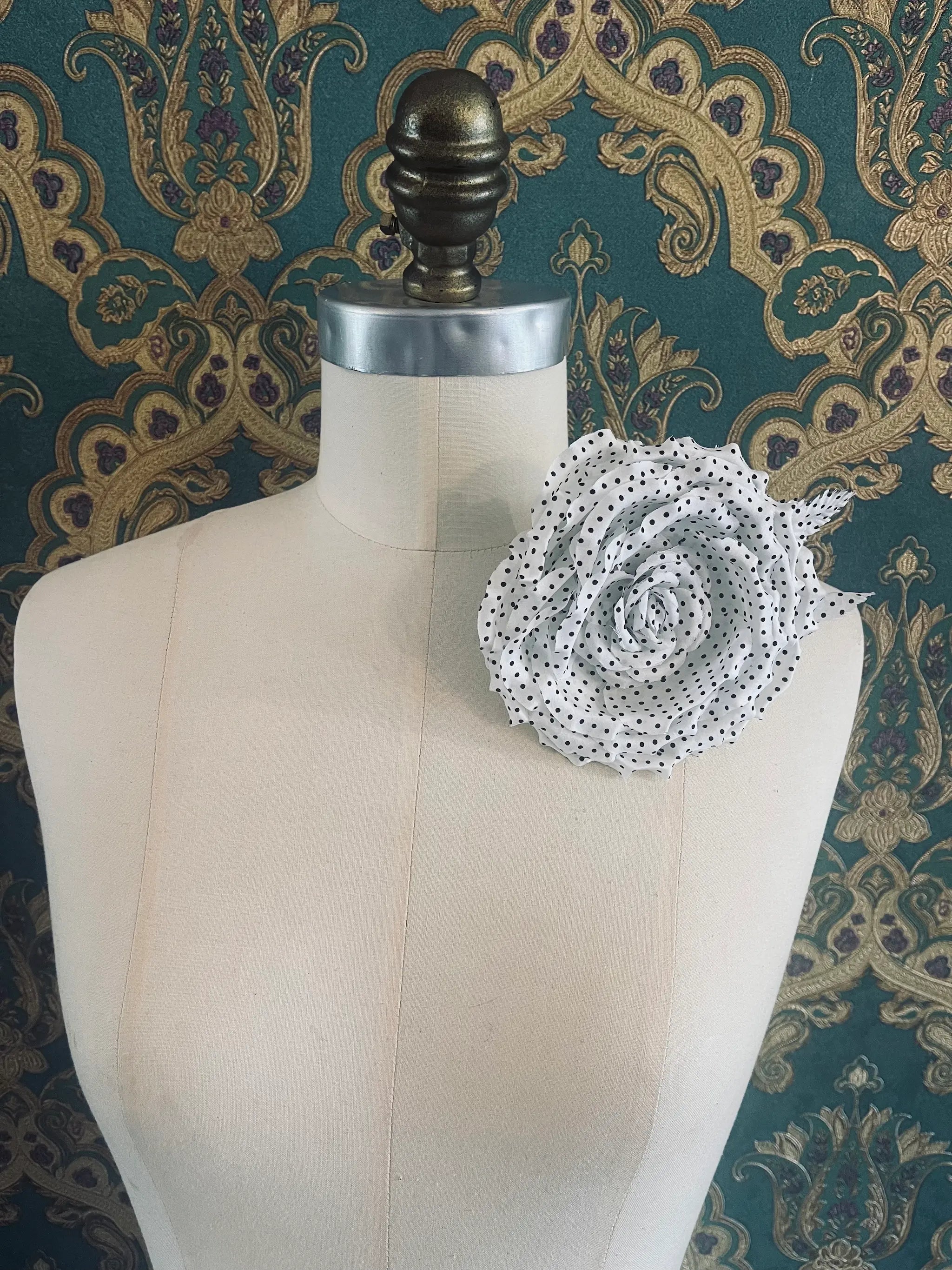 Broochella Dalmata handmade fabric flower brooch in white with black polka dots. Pictured on a mannequin. The background is green and gold damask wallpaper