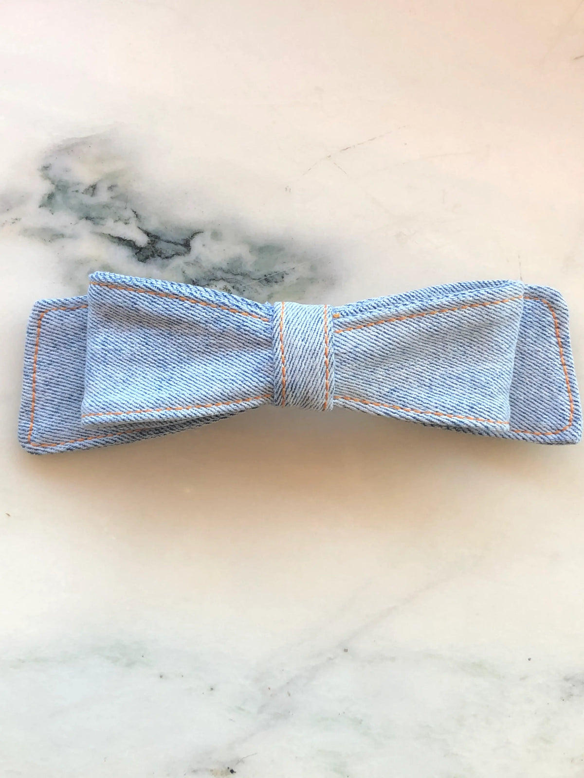  Broochella Denim Hair Bow in light blue denim with contrast tan stitching, photographed on white marble.