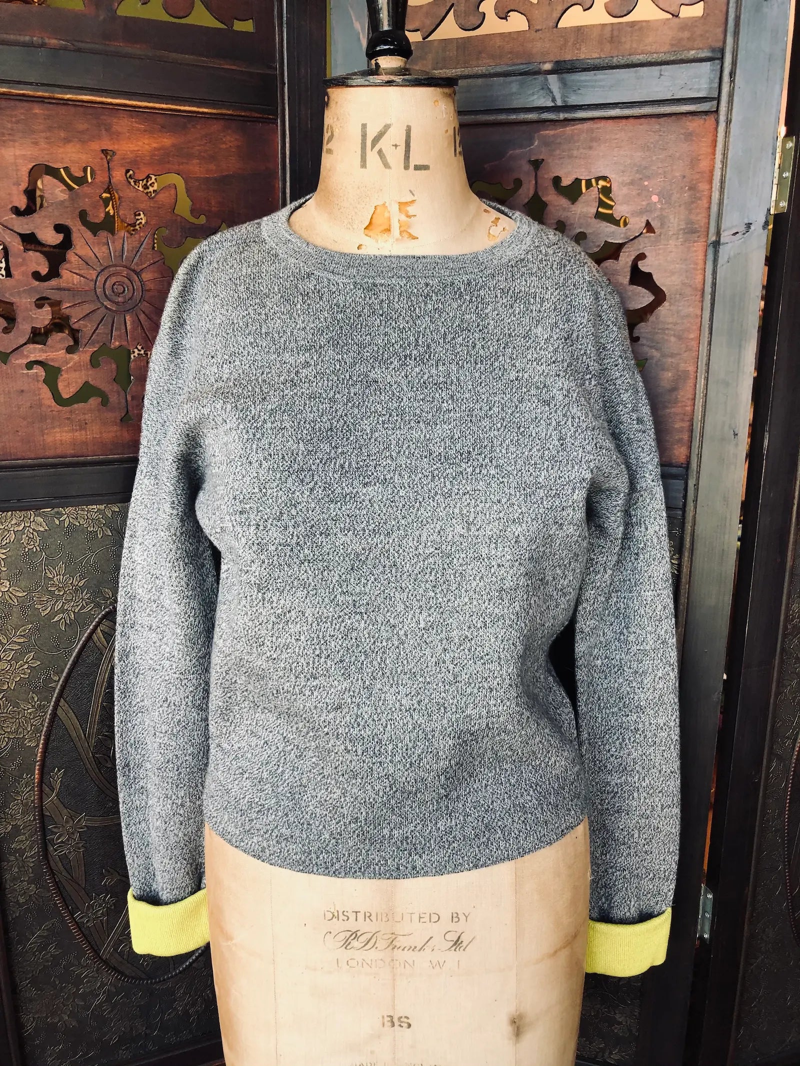 Broochella Derek Lam 10 Crosby sweater.
Size small. It is grey with yellow contrast cuffs. The knit composition is  43% Wool, 42% Cotton, 15% Polyamide. It has a Crew neckline and long sleeves. It is pictured o a vintage mannequin. The background is an ornate, vintage, dark wood room divider. 