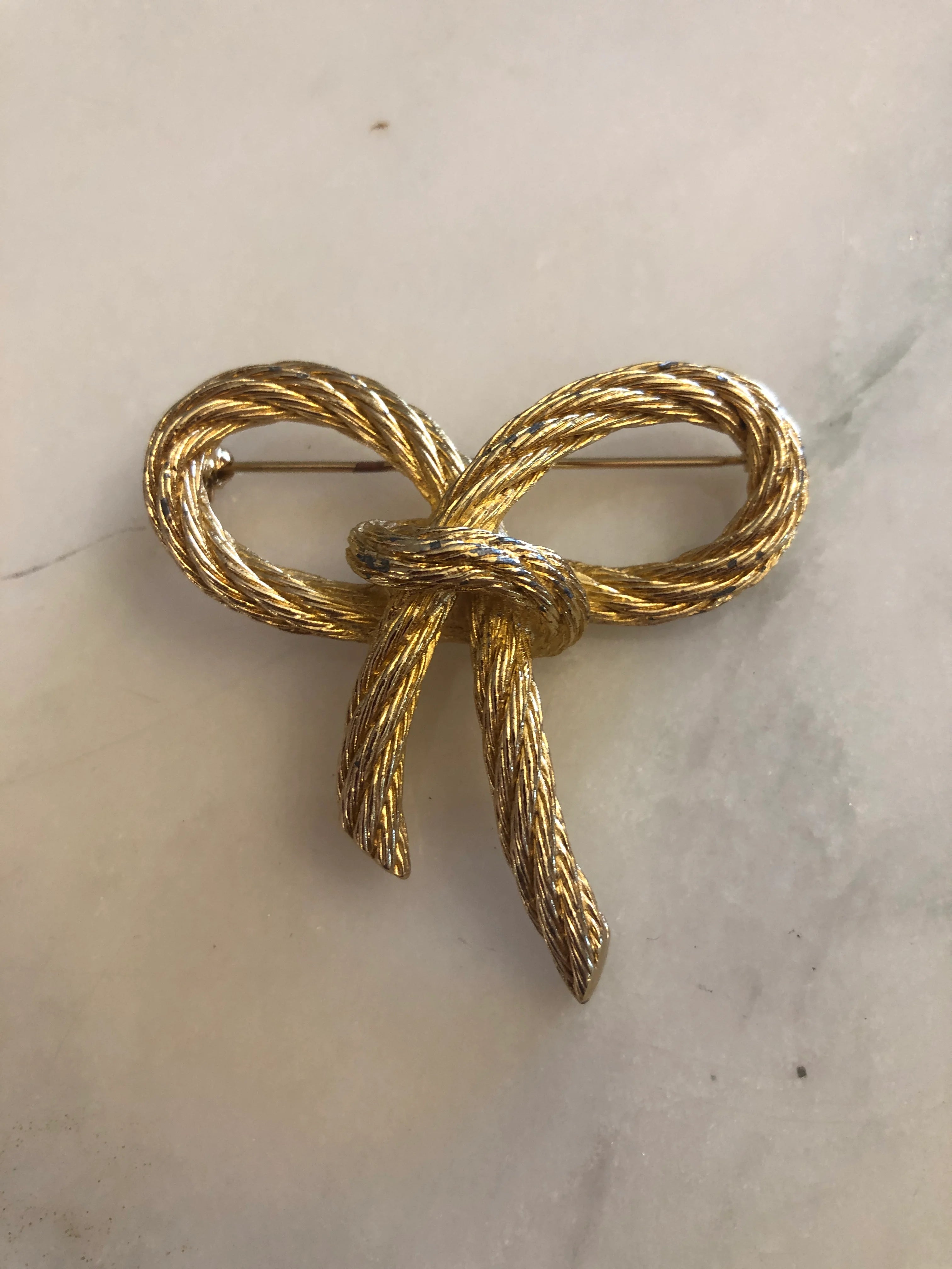 Broochella vintage authentic dior costume bow brooch in gold twisted metal rope.  The background is white marble